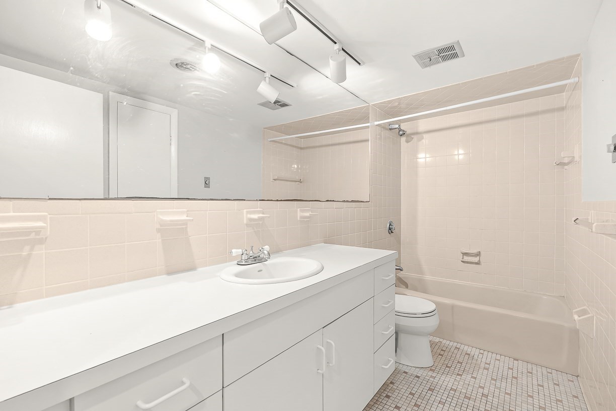 Bathroom with a long white vanity, large mirror, and tub-shower.
