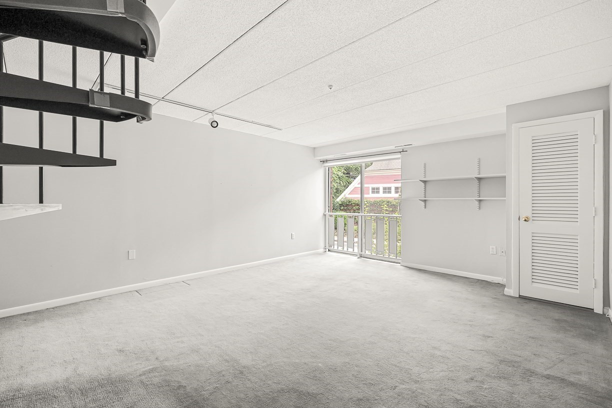 Empty carpeted room with a balcony door, wall shelves, and part of a spiral staircase.