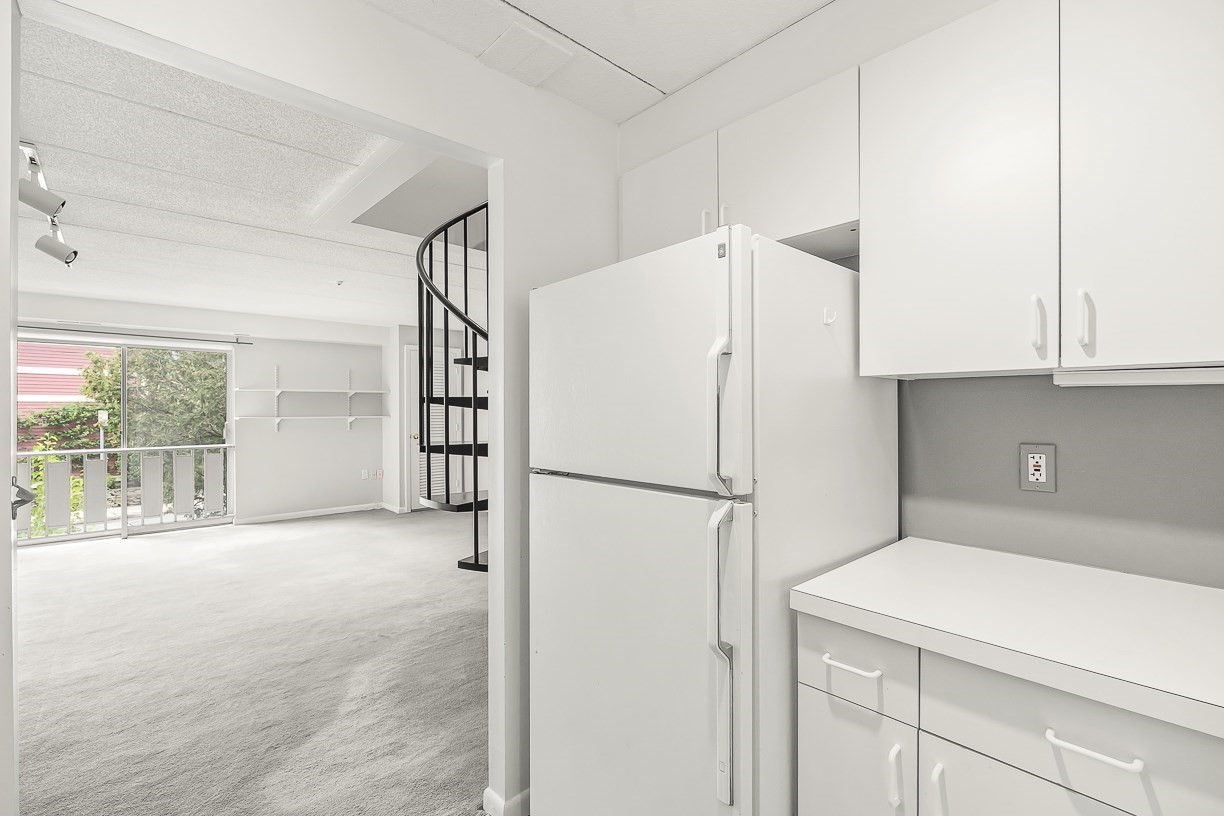 Vacant condo kitchen opening to a carpeted living area with a black spiral staircase.