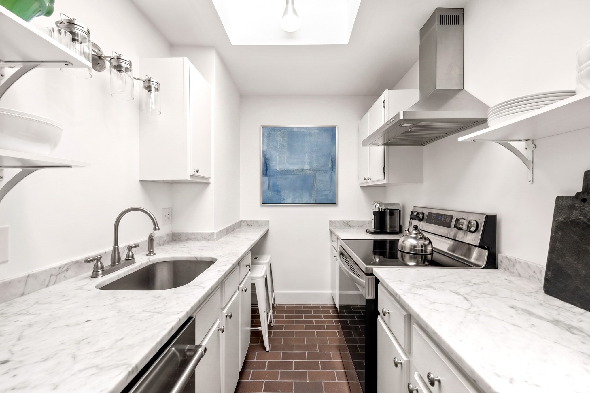 Bright kitchen with marble counters, stainless-steel appliances, brick flooring, and a skylight.