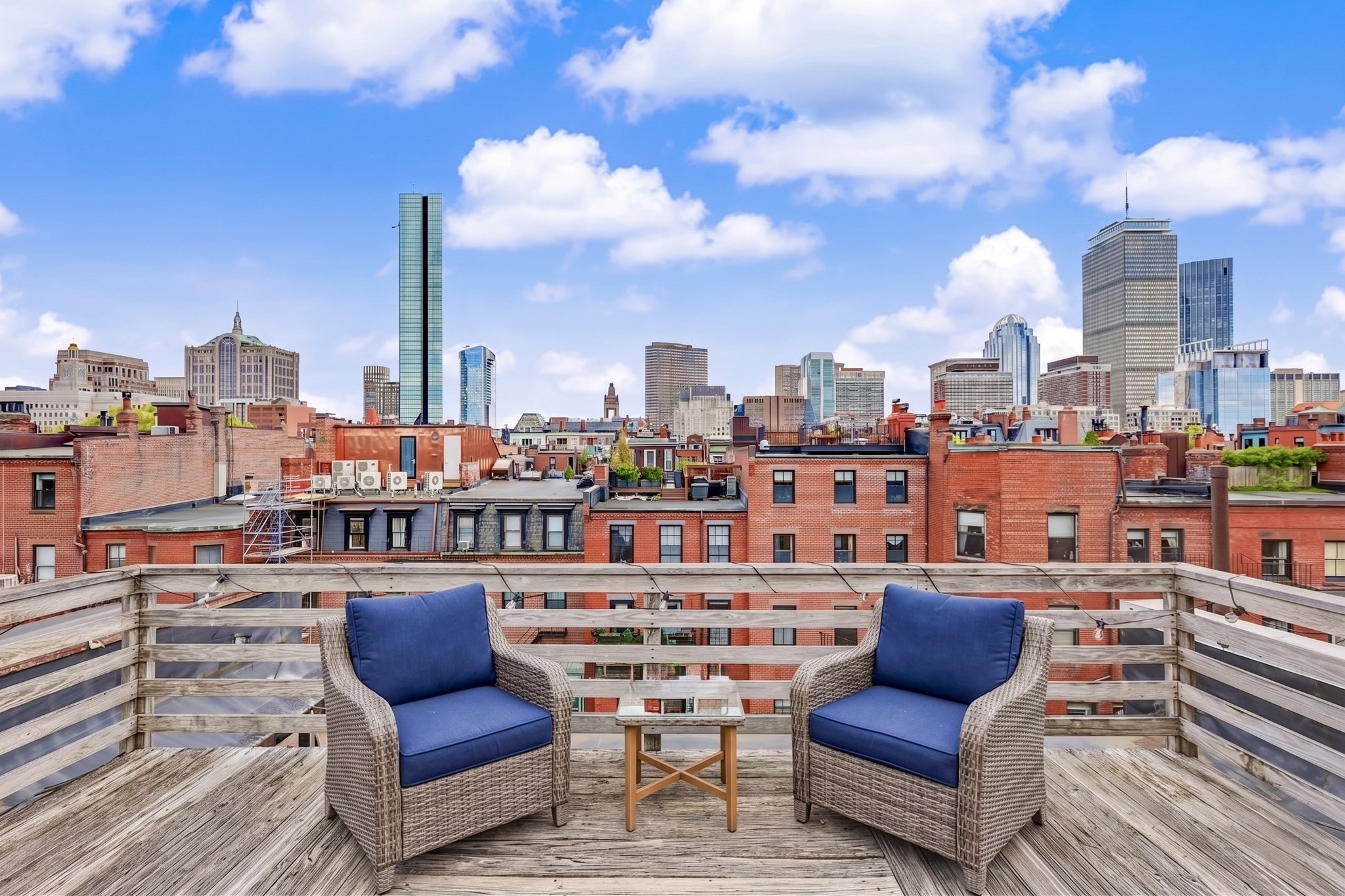 Rooftop deck with two blue-cushioned wicker chairs overlooking Boston’s skyline.