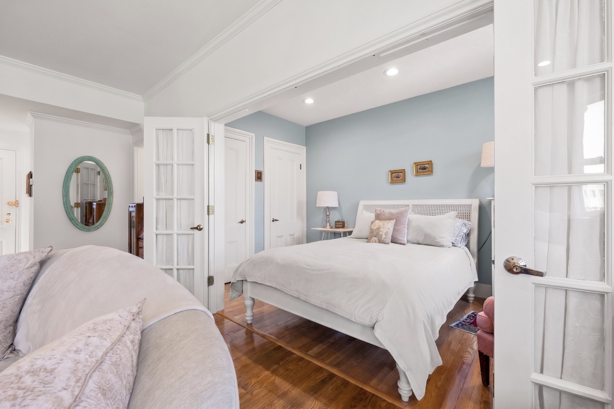 Bedroom with a white bed, pale blue accent wall, hardwood floors, and French doors.