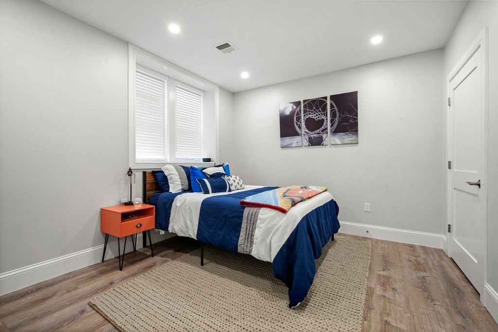 Furnished bedroom with a blue-and-white bed, orange bedside table, and large window with blinds.