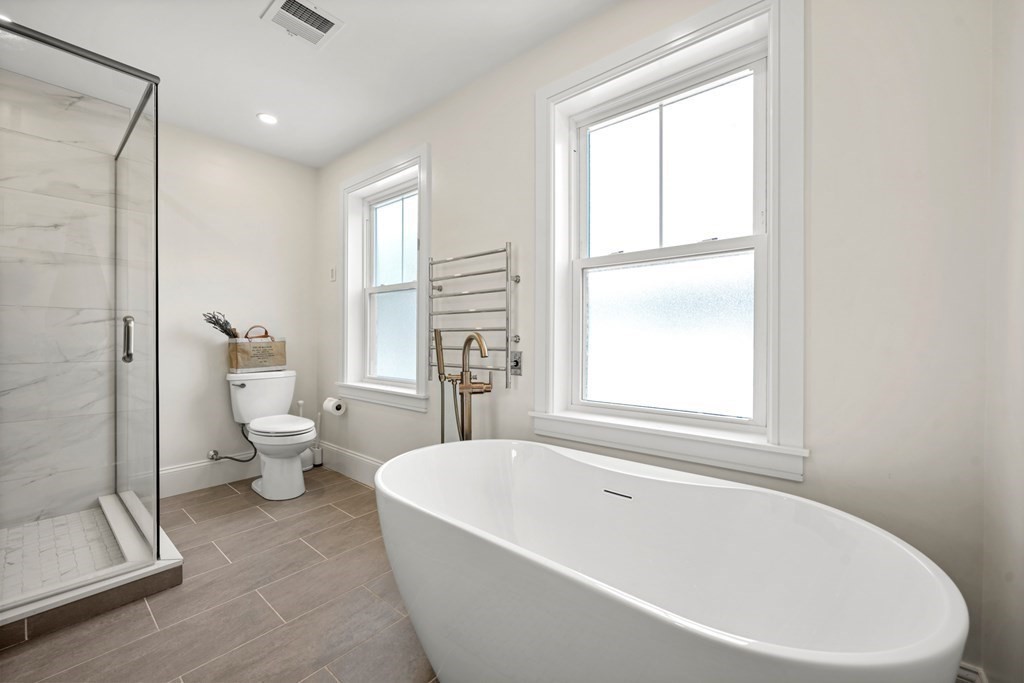 Bright bathroom with a freestanding soaking tub, glass shower, and heated towel rack.