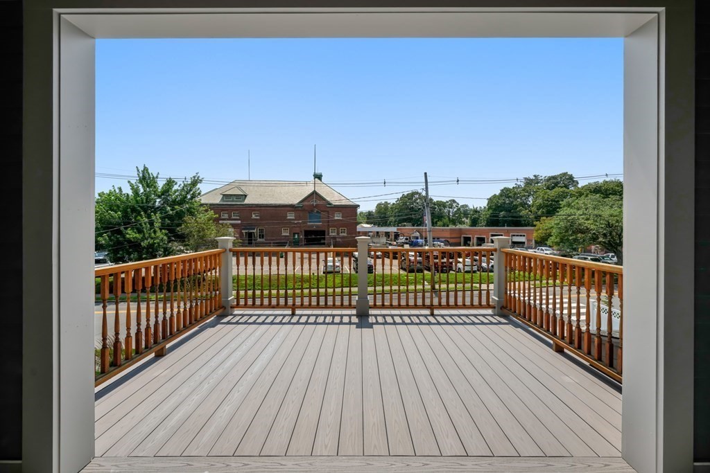 Unfurnished deck with wood railings overlooking trees, parked cars, and brick buildings.