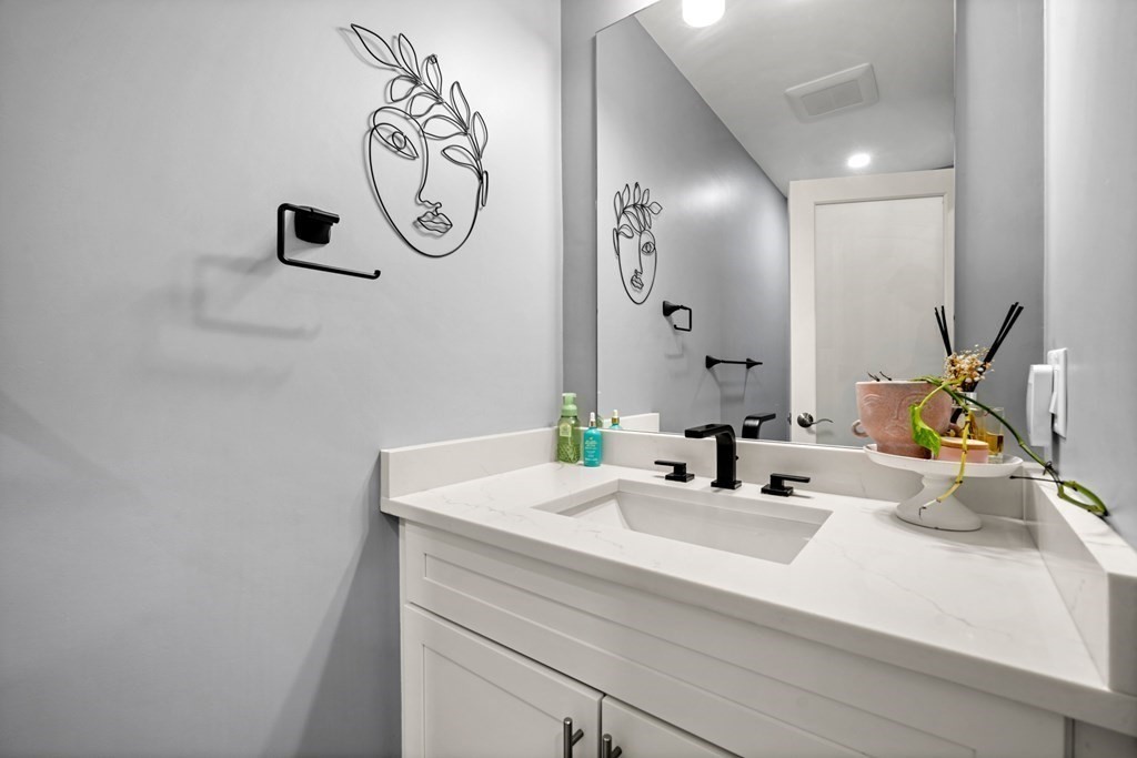 Modern bathroom vanity with a white sink, black fixtures, and face-shaped wall art.