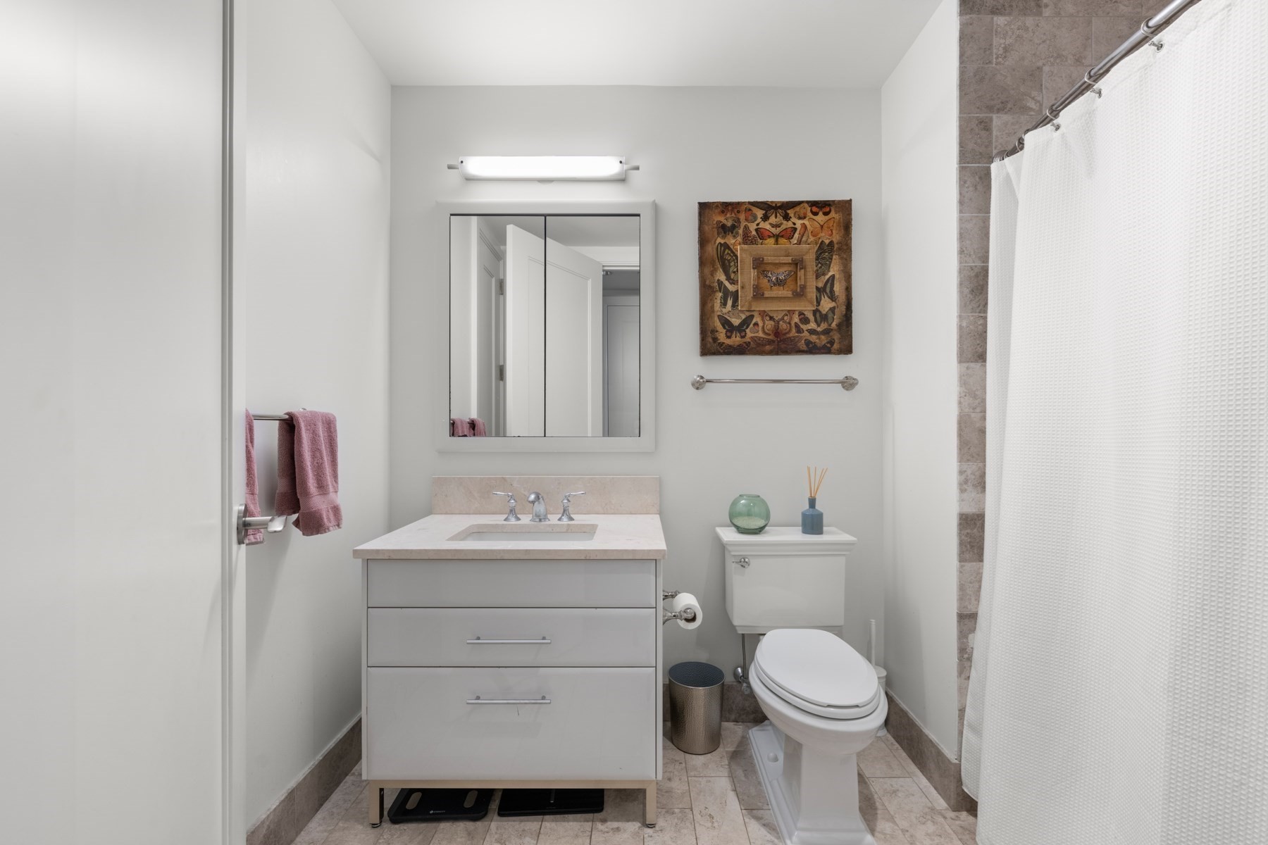 Bathroom with a white vanity, mirrored cabinet, toilet, and tiled shower with a white curtain.