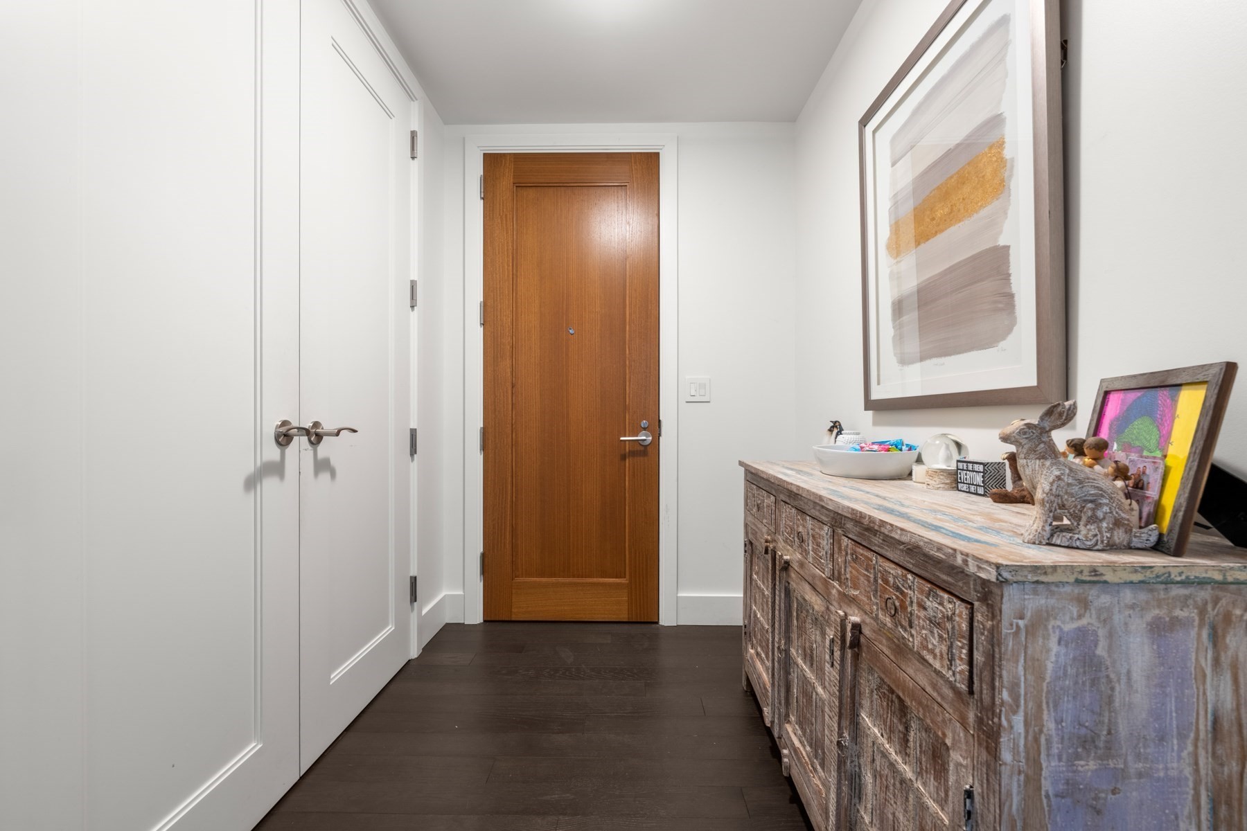 Apartment entryway with a wooden front door, white closets, and a rustic console table.
