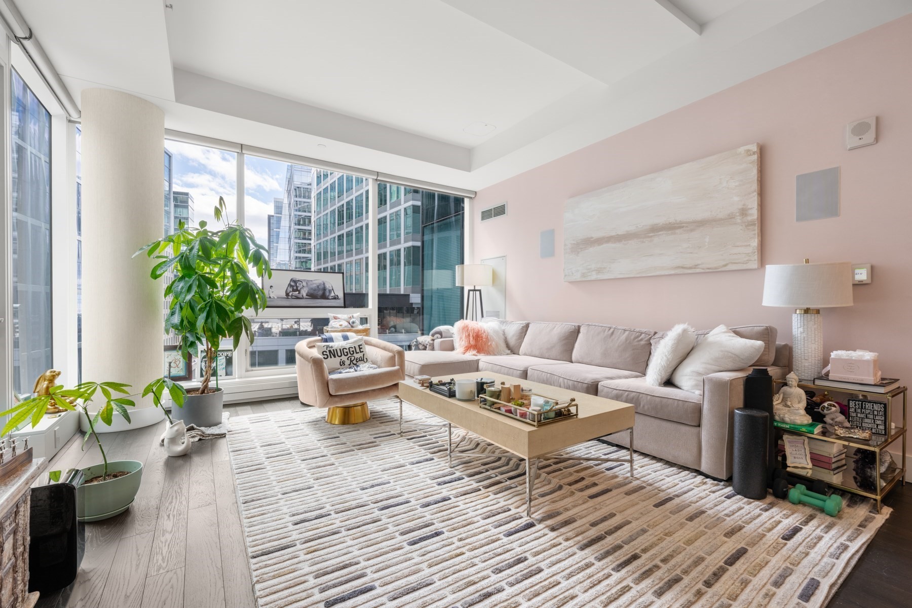 Living room with floor-to-ceiling windows, a large sectional sofa, and city buildings outside.