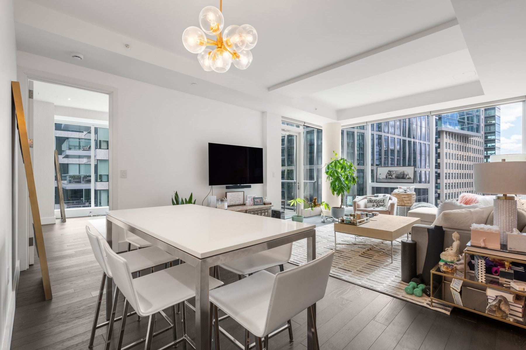 Open-plan condo living and dining area with floor-to-ceiling windows and nearby city buildings.