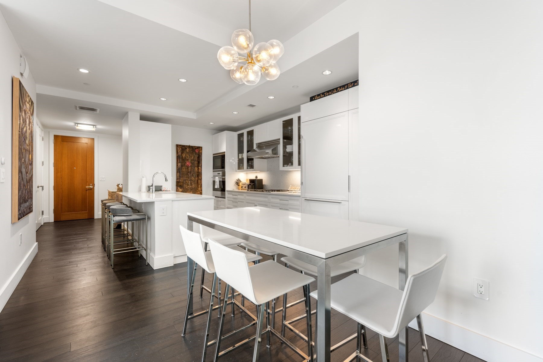 Modern white kitchen and dining area with an island, bar stools, and dark wood floors.
