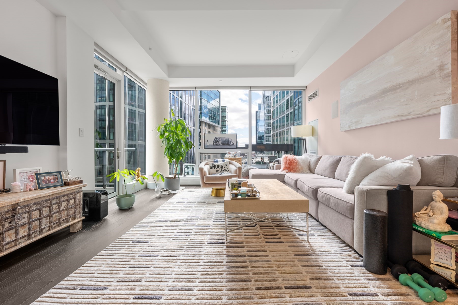 Furnished condo living room with floor-to-ceiling windows overlooking glass city buildings.