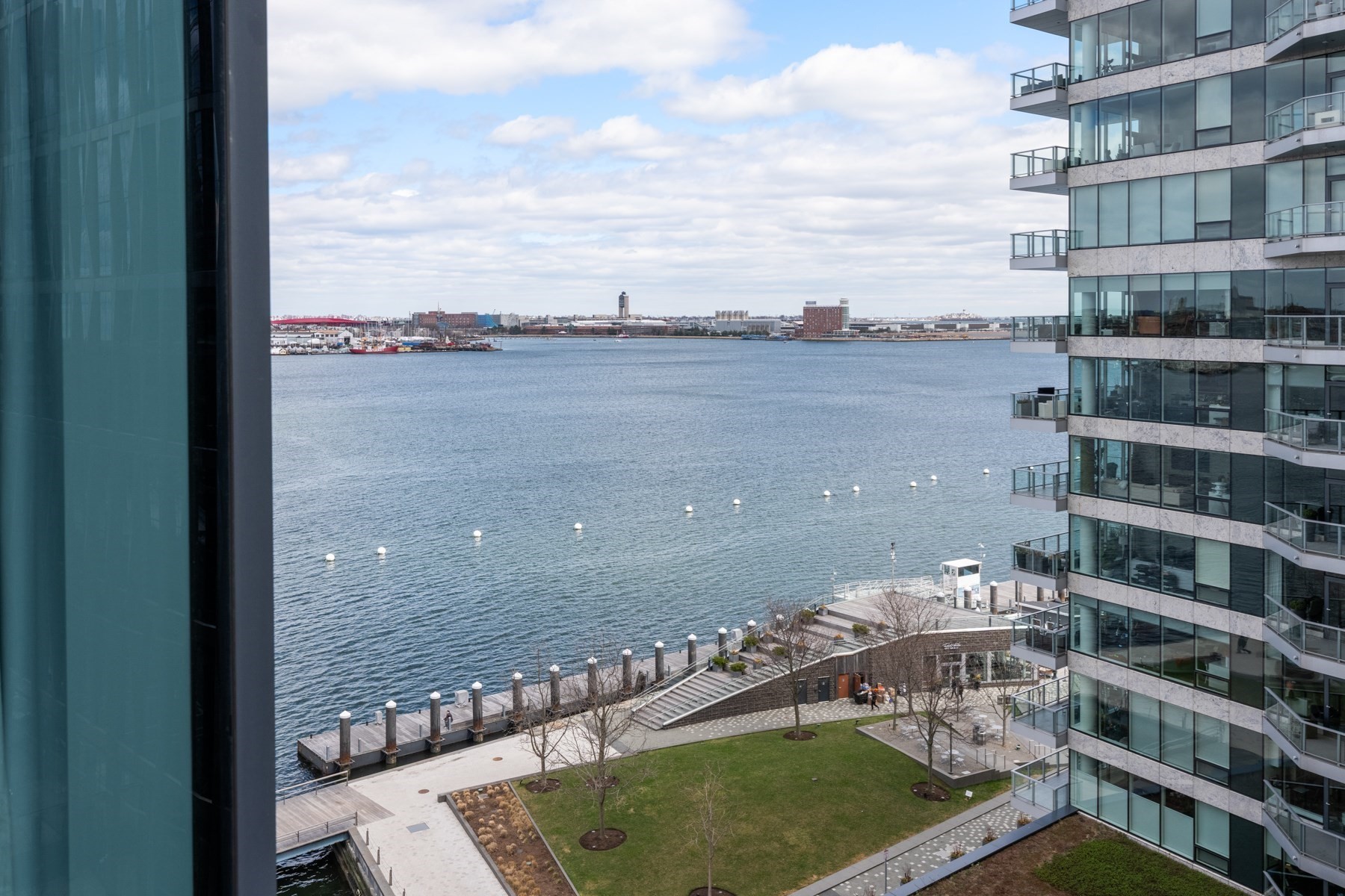 Harbor view from a high-rise residence, framed by glass towers and a landscaped waterfront promenade.