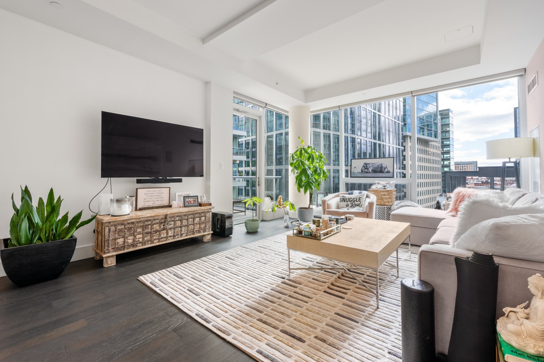 Bright living room with floor-to-ceiling windows overlooking glass office towers.