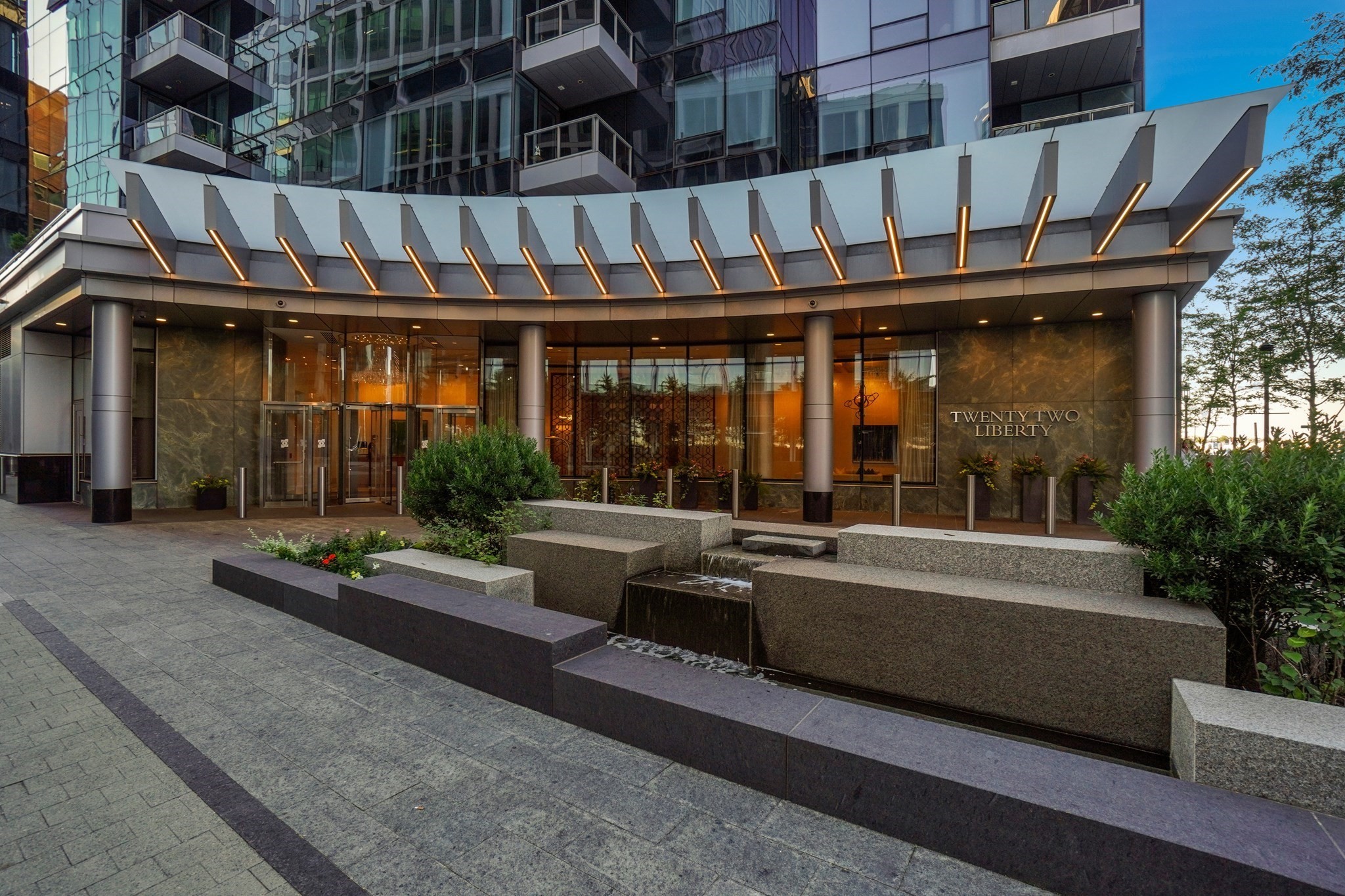 Twenty Two Liberty entrance with a curved canopy, glass lobby, landscaped planters, and stone water feature.