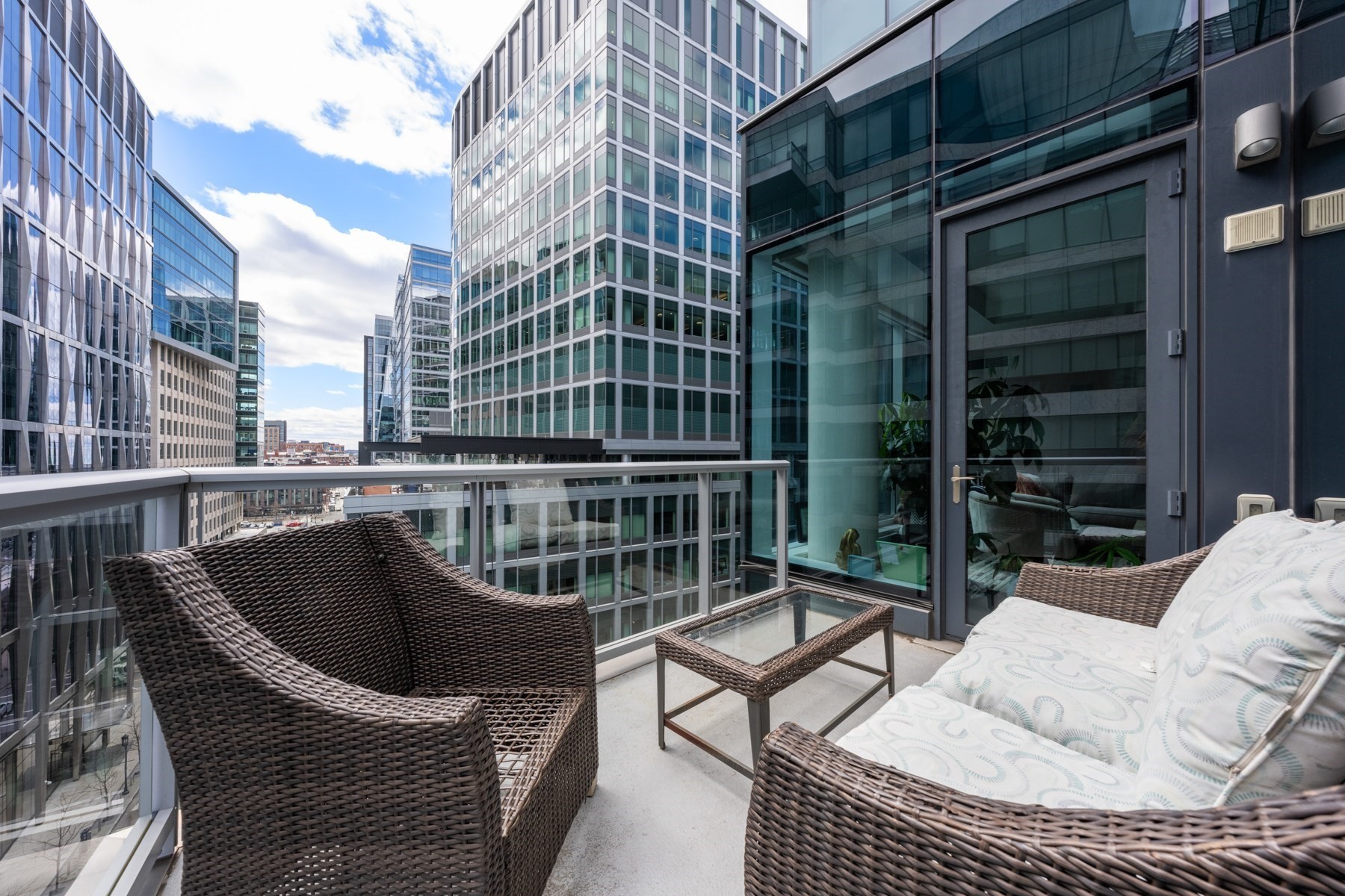 Furnished balcony with wicker seating and views of modern downtown Boston buildings.