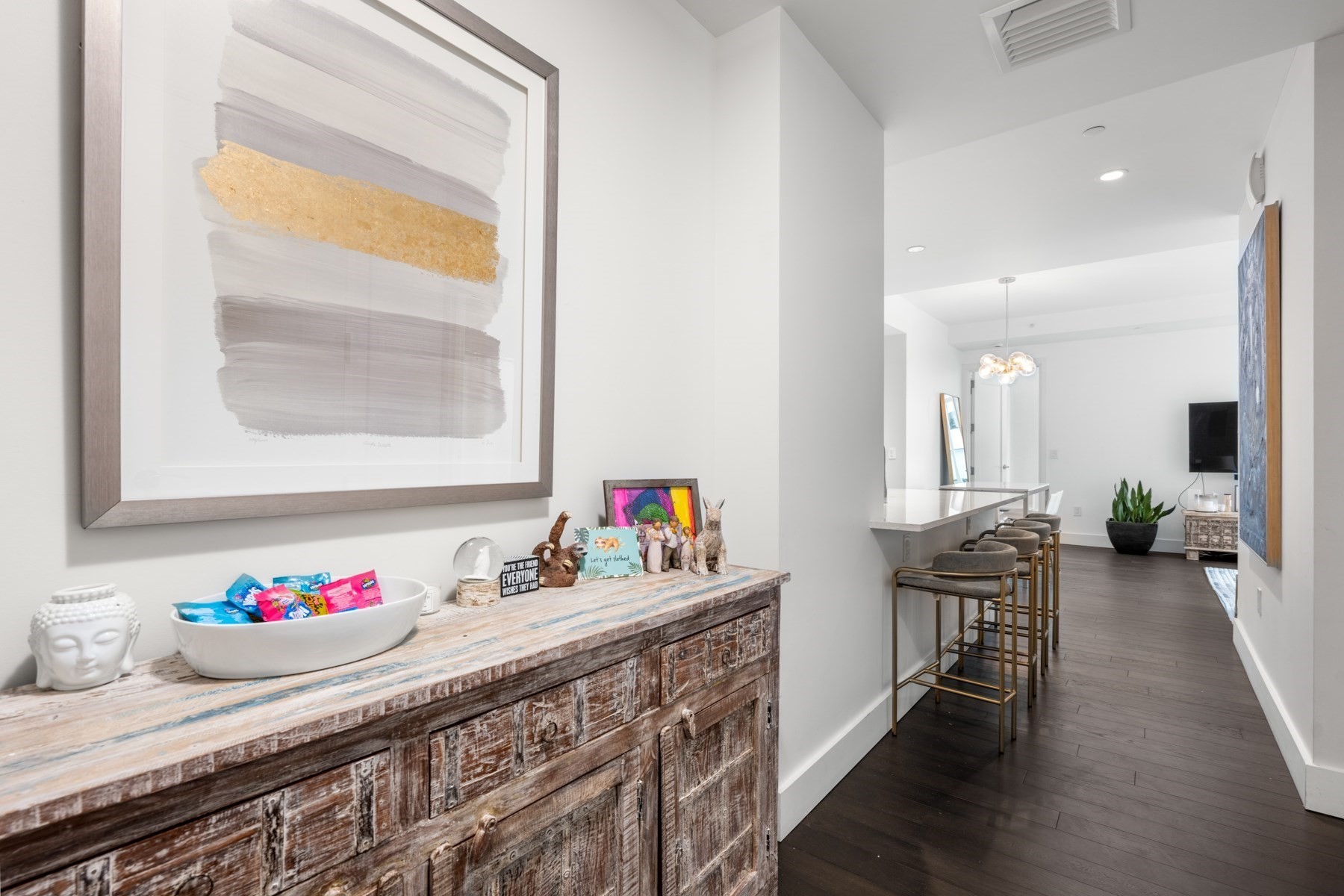 Furnished condo entry hall with a rustic wood console, abstract artwork, and a kitchen island with bar stools.
