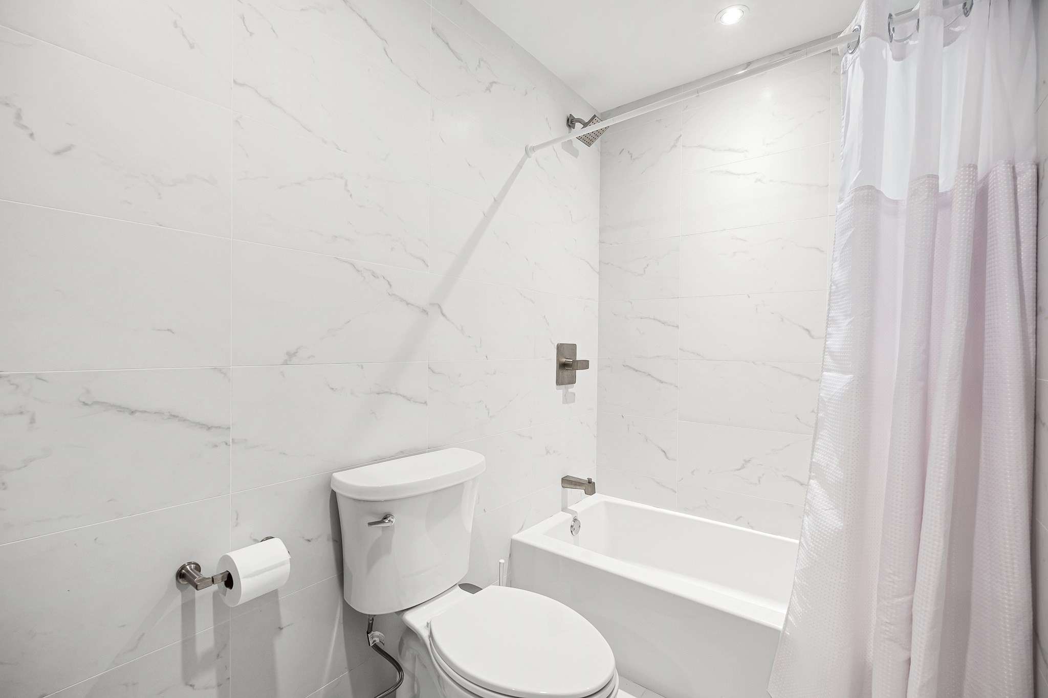Modern bathroom with marble-look tile, a bathtub and shower curtain, and a toilet.