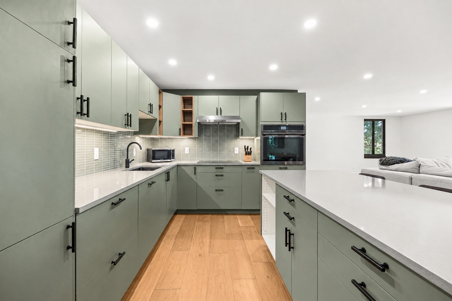 Modern sage-green kitchen with a large white island and open view to the living area.