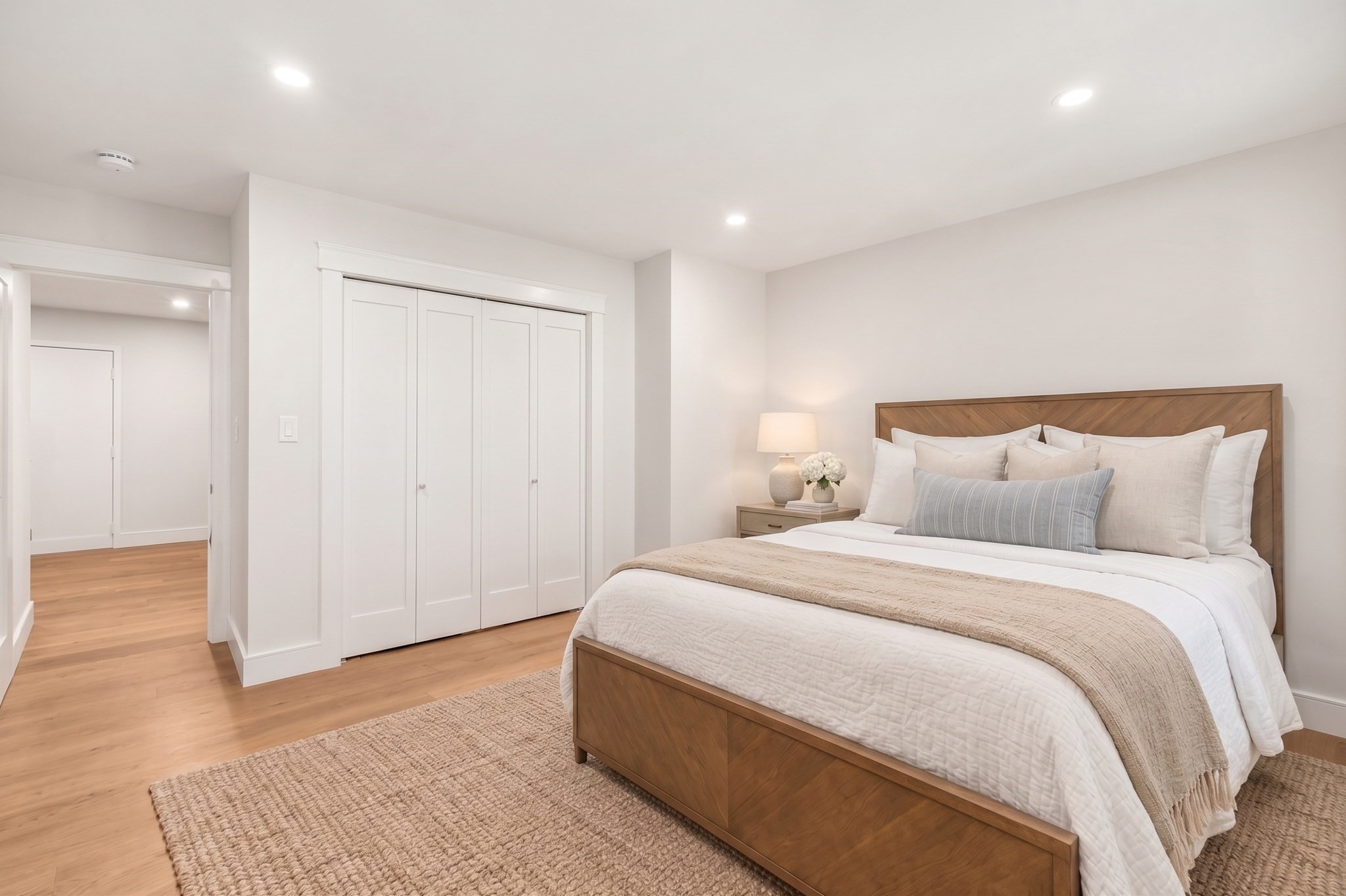 Staged bedroom with a wood-framed bed, white bedding, a large closet, and light wood floors.