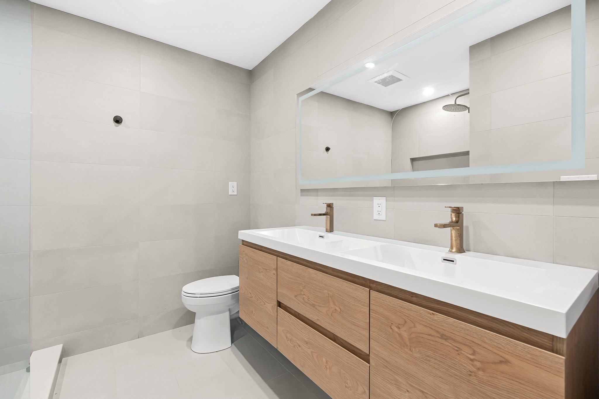 Modern bathroom with a double-sink wood vanity, large mirror, and pale tile walls.