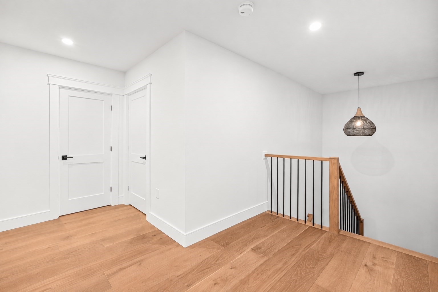 Bright upstairs landing with oak floors, white paneled doors, and a black metal stair railing.