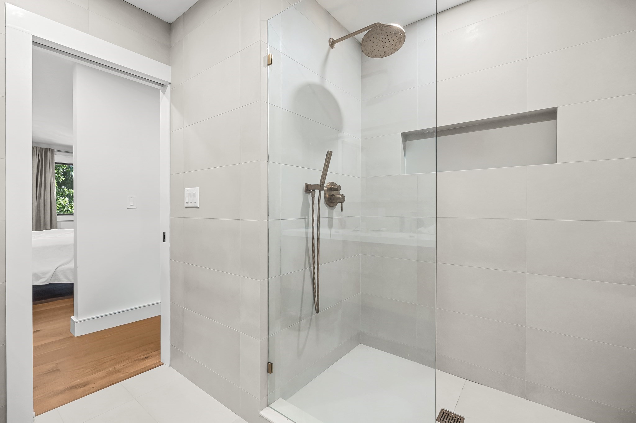 Modern tiled bathroom with a glass walk-in shower, rainfall showerhead, and recessed wall niche.