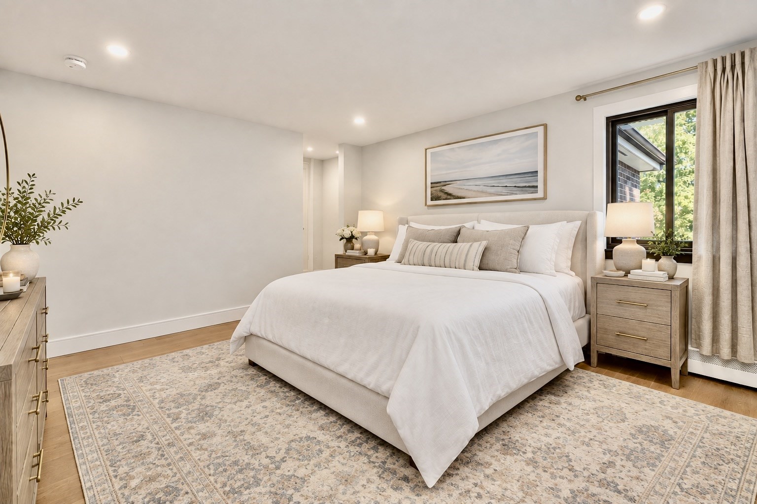 Staged bedroom with a white bed, patterned rug, wood nightstands, and a sunny window.