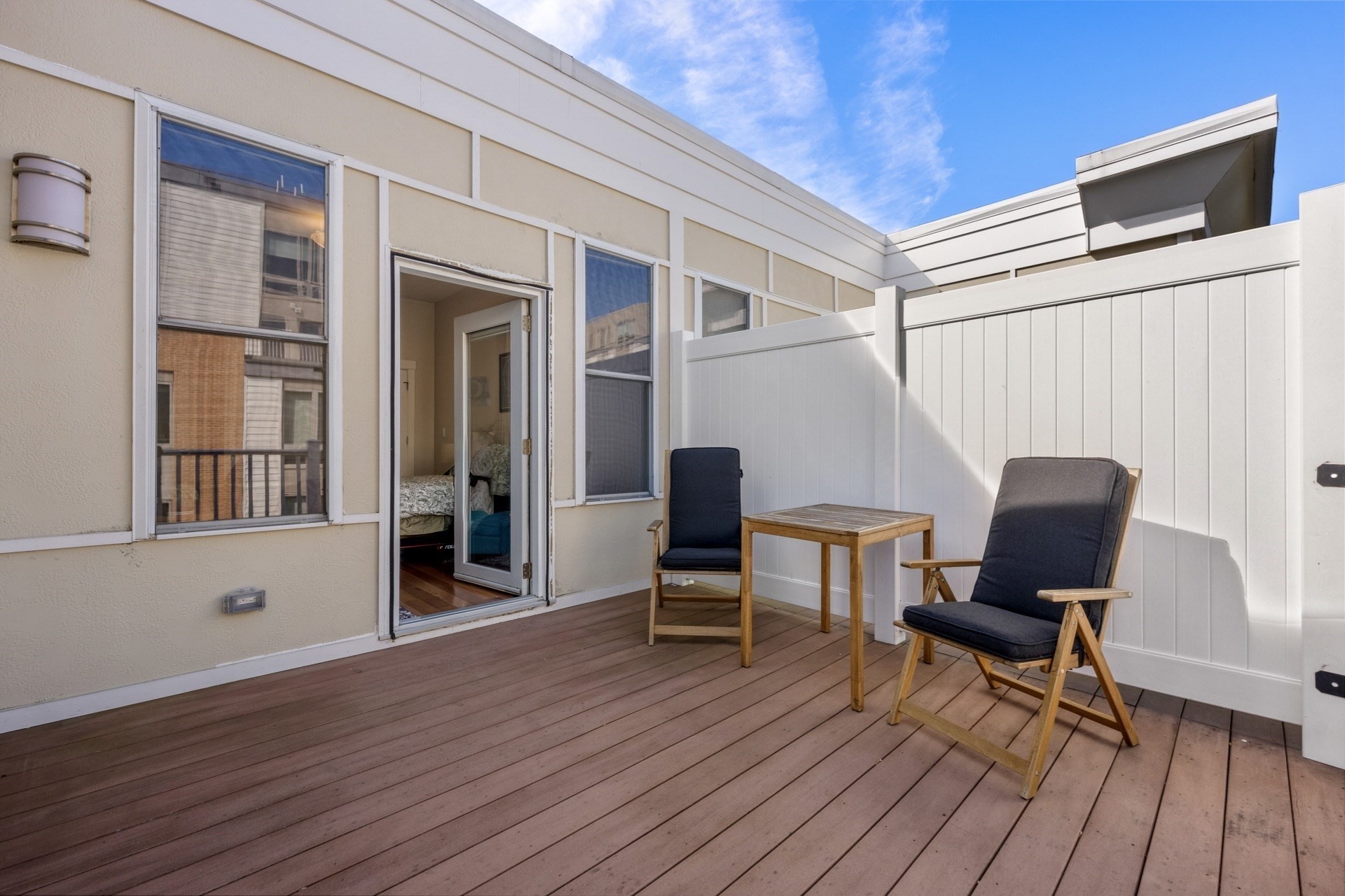 Private rooftop deck with two cushioned chairs and a wooden table beside an open apartment door.