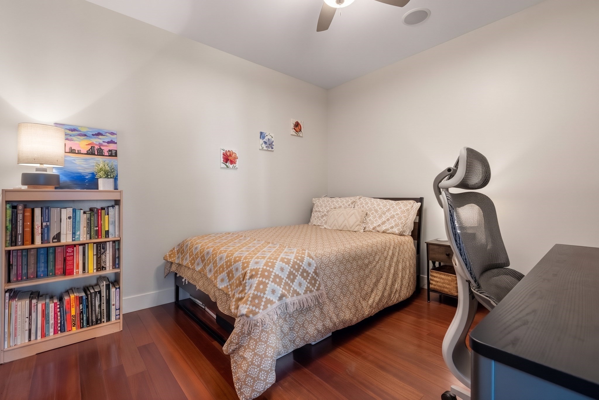 Bedroom with patterned bedding, a full bookcase, and an ergonomic desk chair.