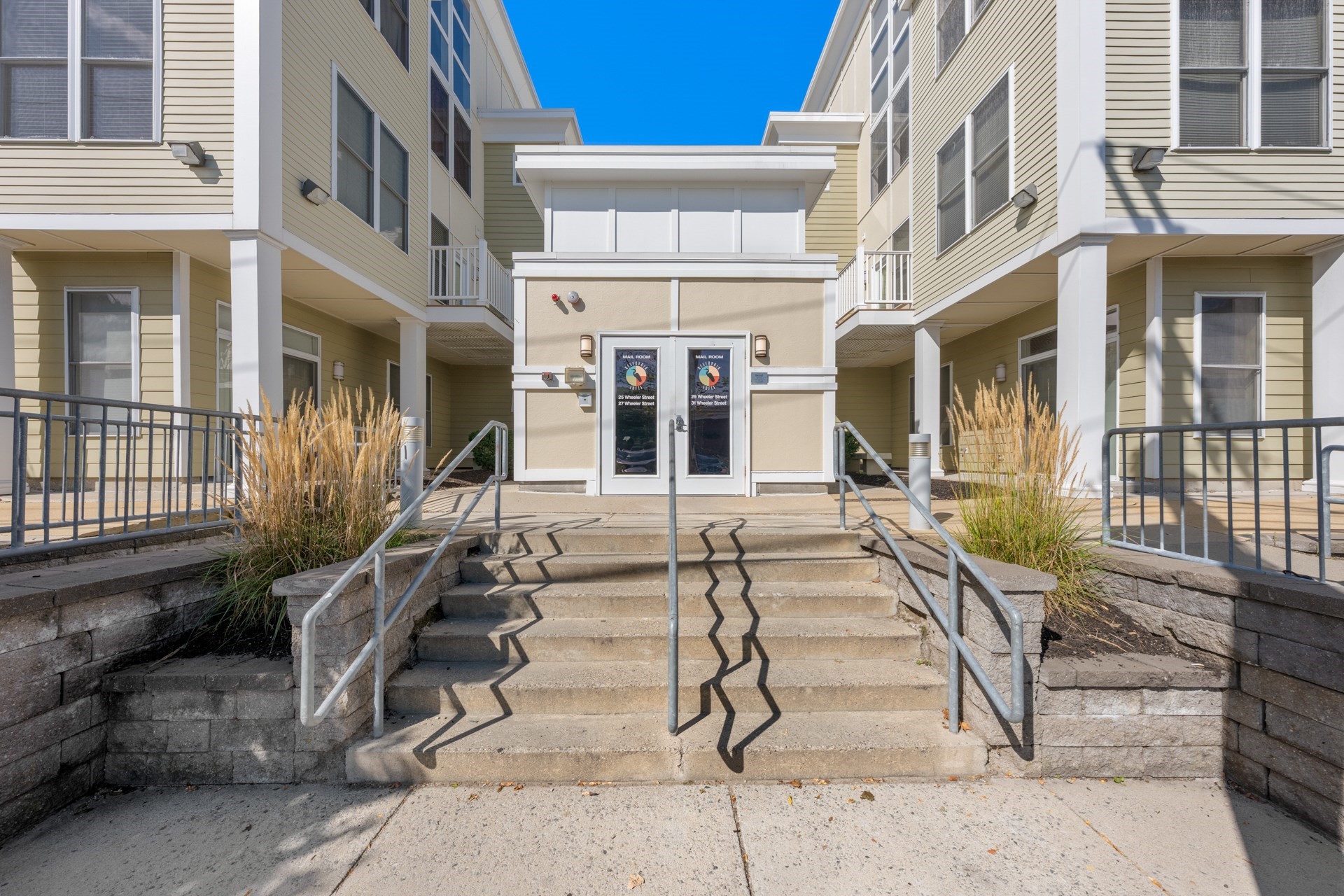 Residential building entrance with concrete steps, metal railings, and central mail room doors.