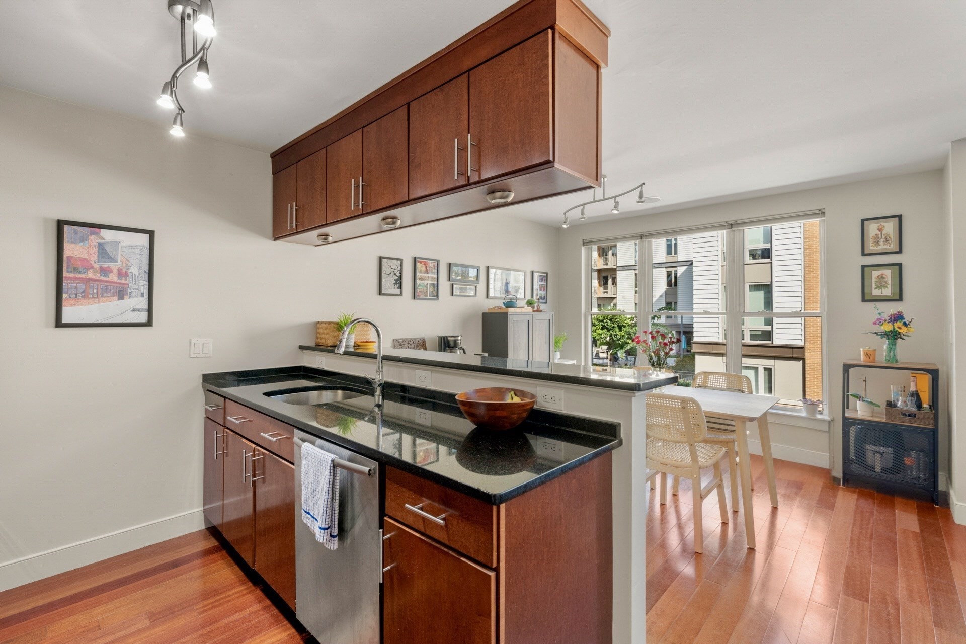 Condo kitchen with cherry wood cabinets, black counters, and a dining nook beside large windows.