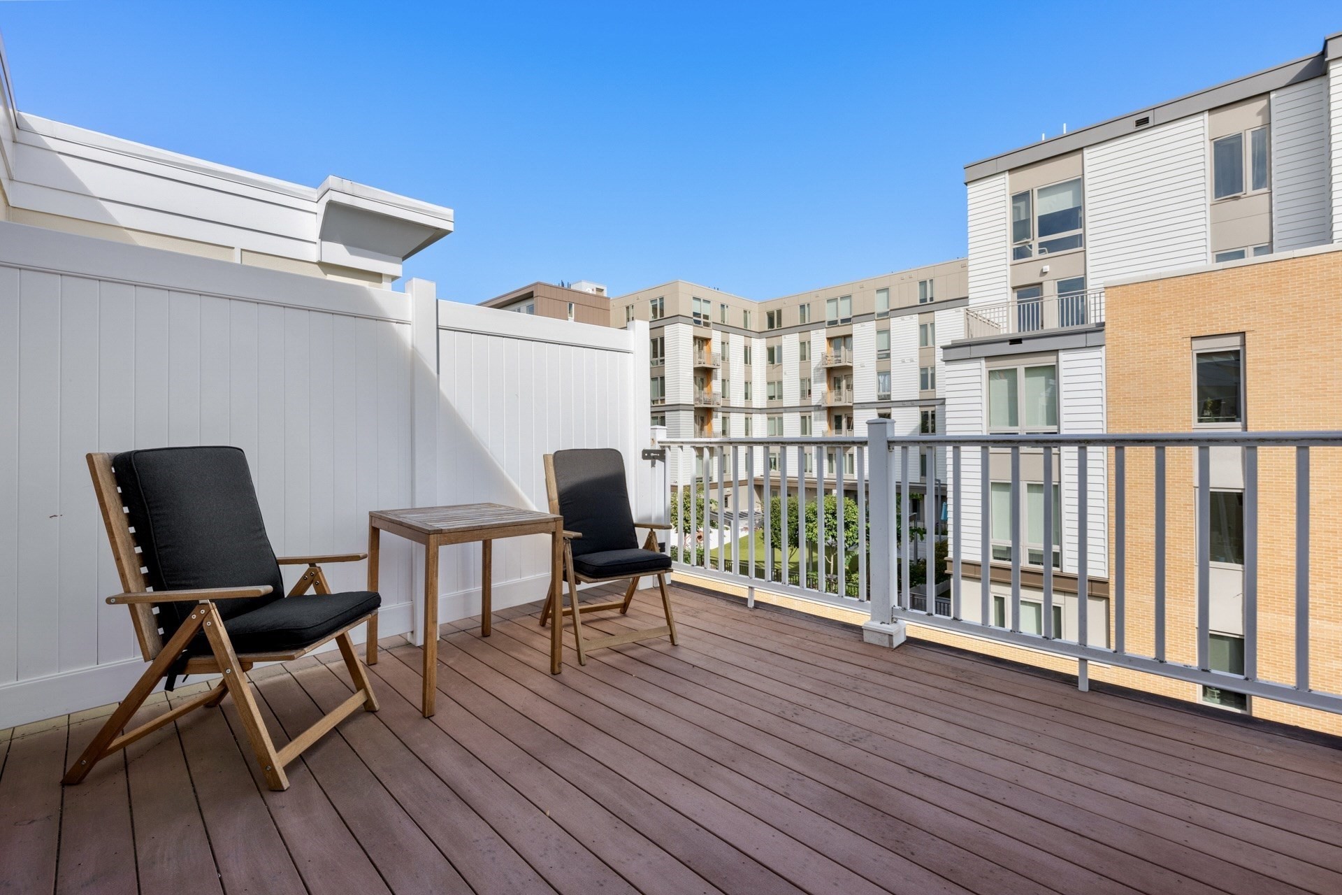 Furnished apartment deck with two chairs overlooking a courtyard and modern residential buildings.