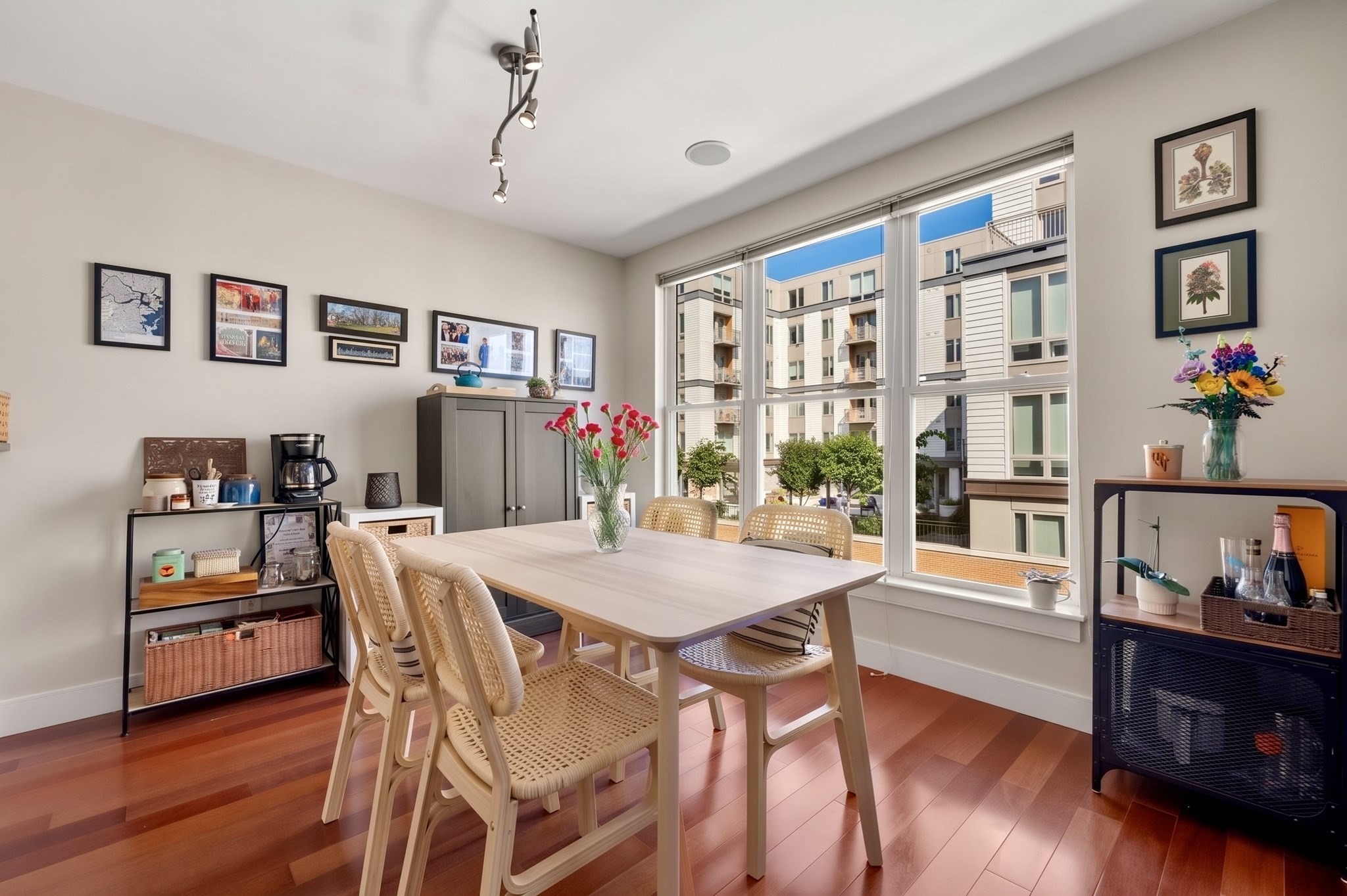 Dining room with a light wood table, woven chairs, hardwood floors, and large windows.