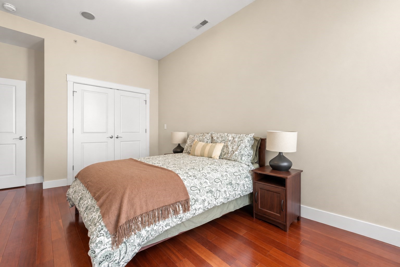Bedroom with a patterned bedspread, brown throw, and reddish hardwood floors.