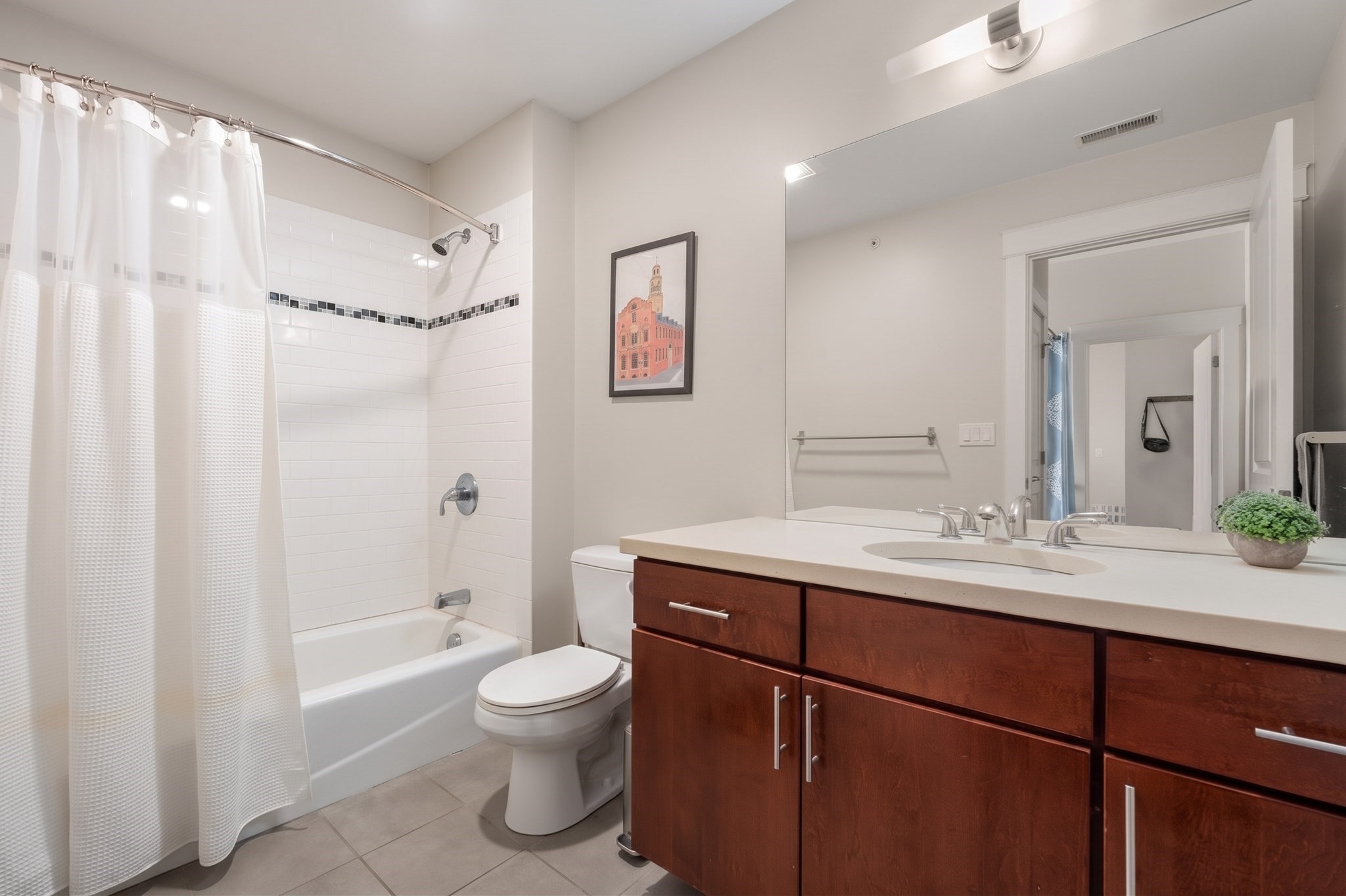 Bathroom with a tiled tub-shower, dark wood vanity, and large wall mirror.