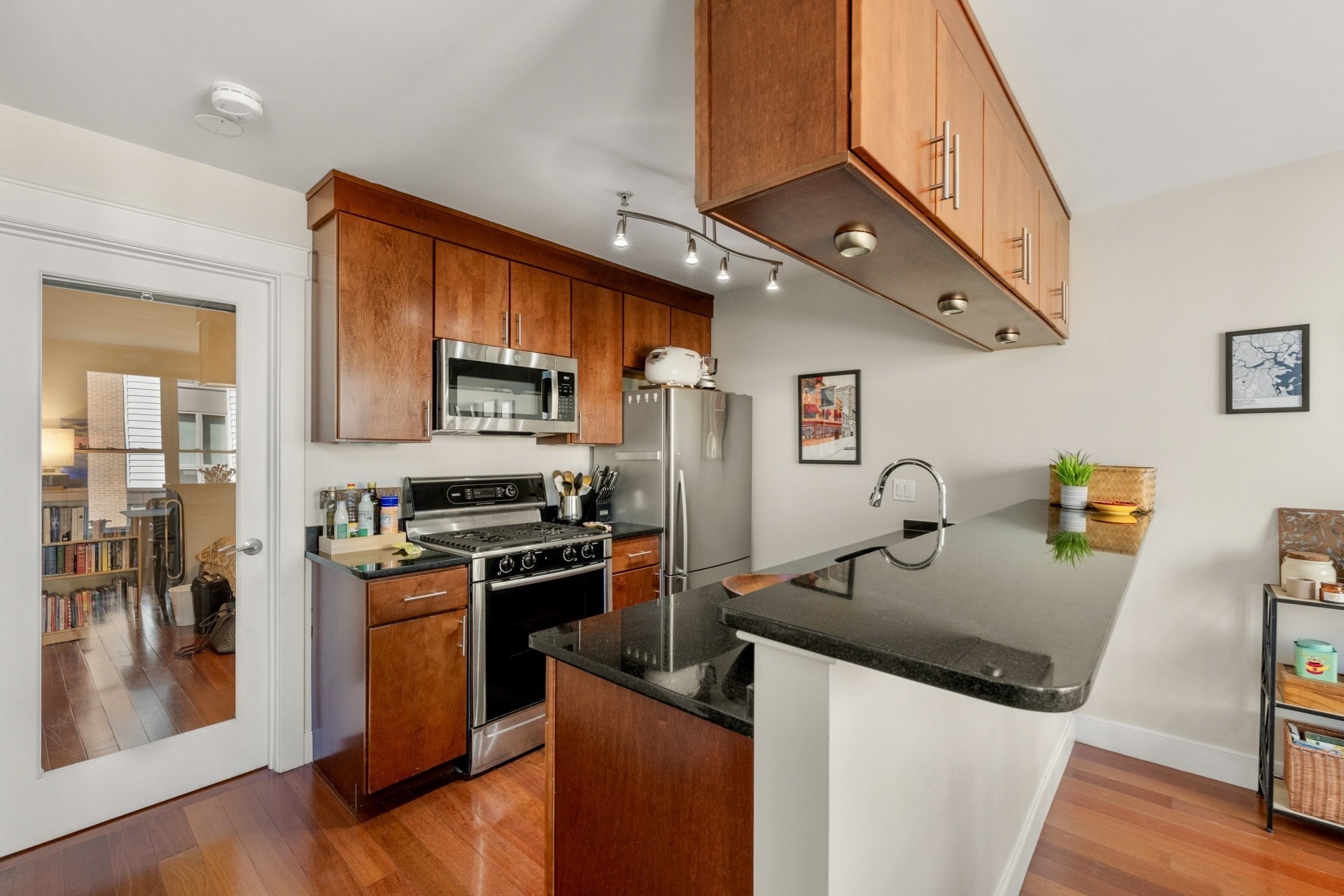 Condo kitchen with warm wood cabinets, stainless steel appliances, and a large black stone island.