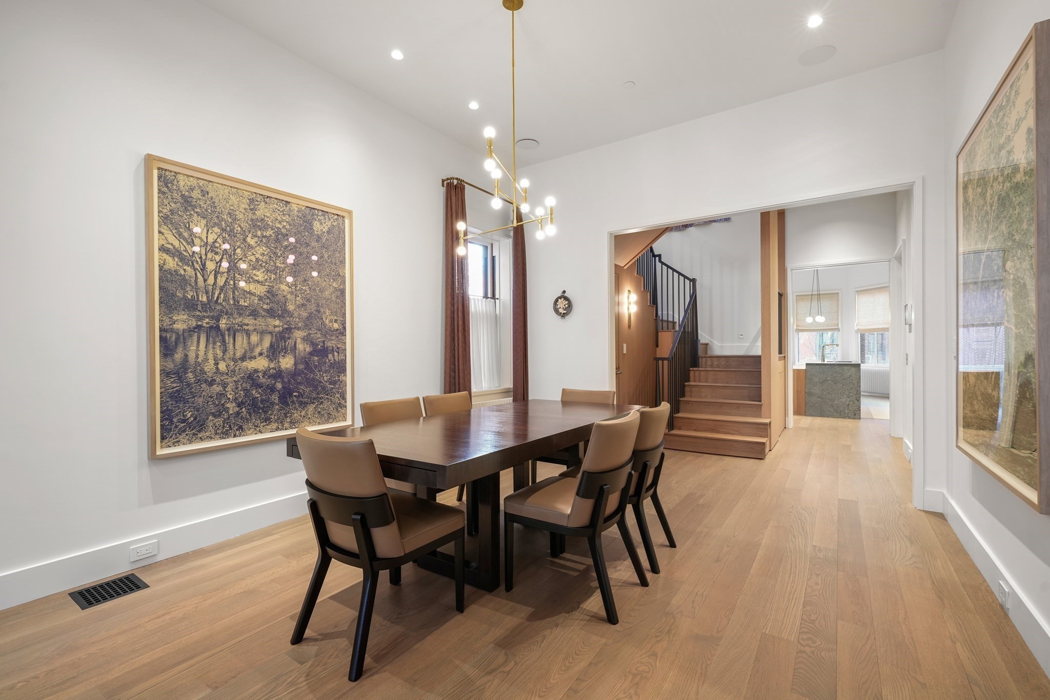 Dining room with a dark wood table, tan chairs, brass chandelier, and open view to a staircase.