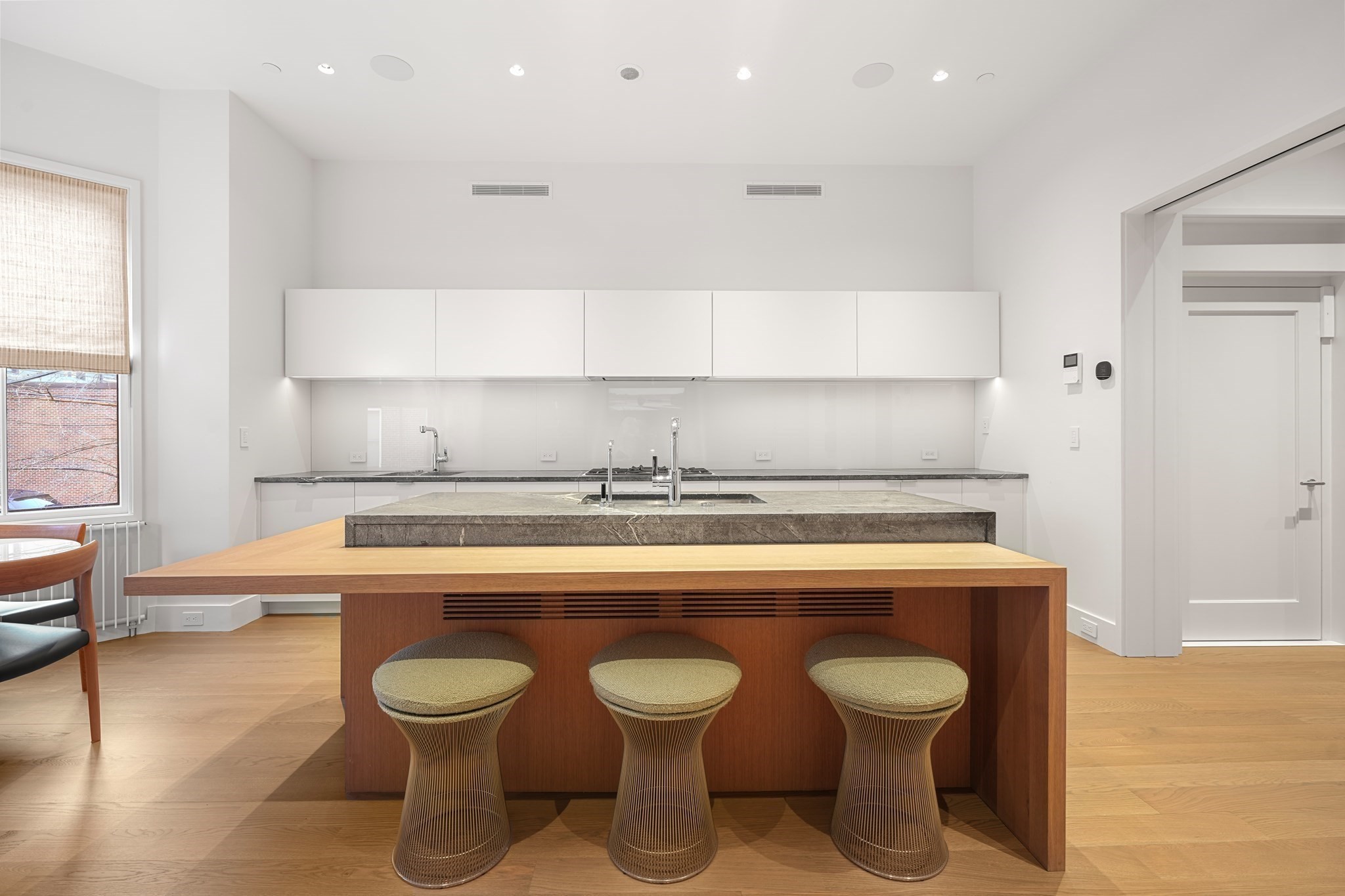 Modern kitchen with a wood island, three stools, white cabinets, and stone counters.