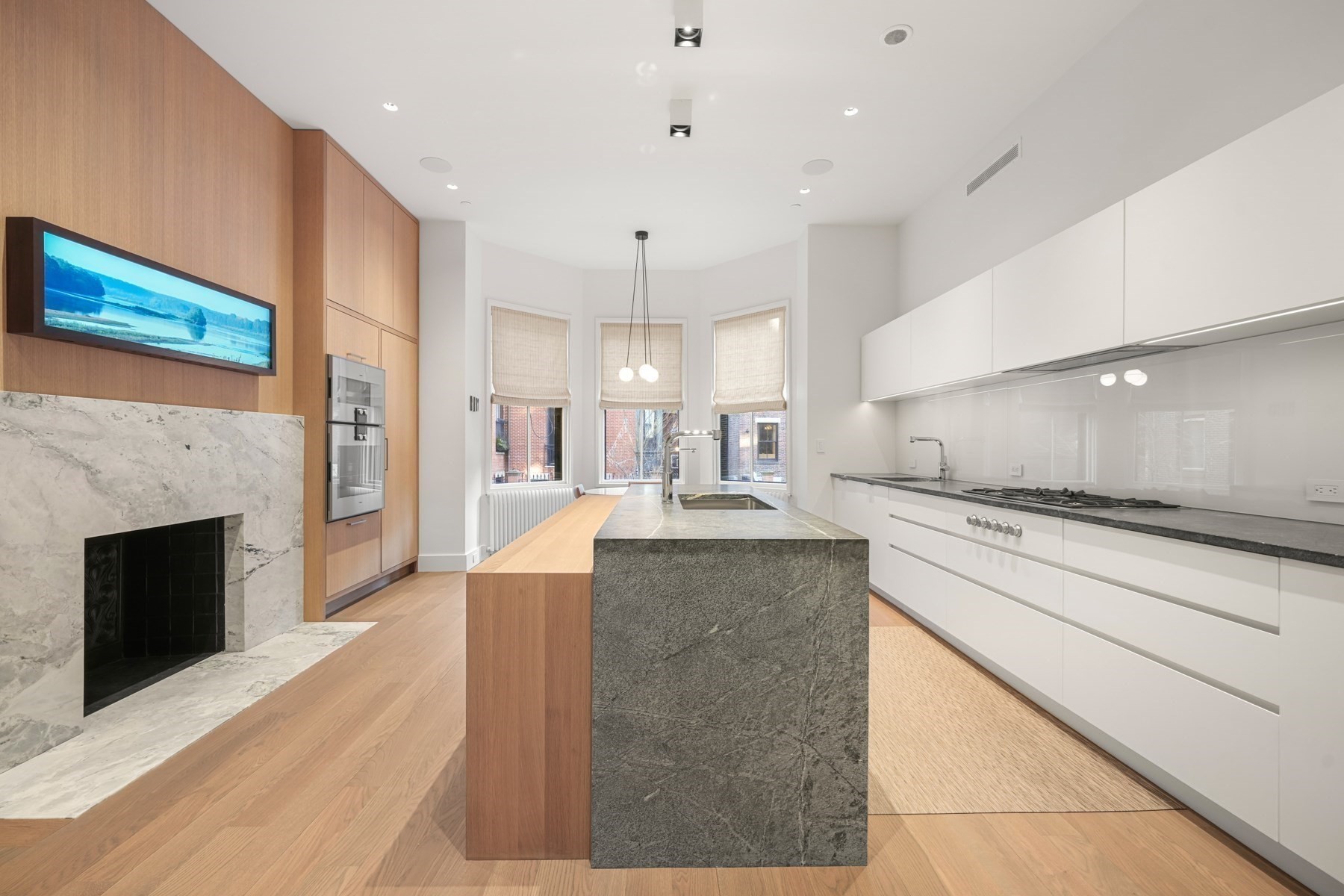 Modern kitchen with a large stone island, white cabinetry, and a marble fireplace.