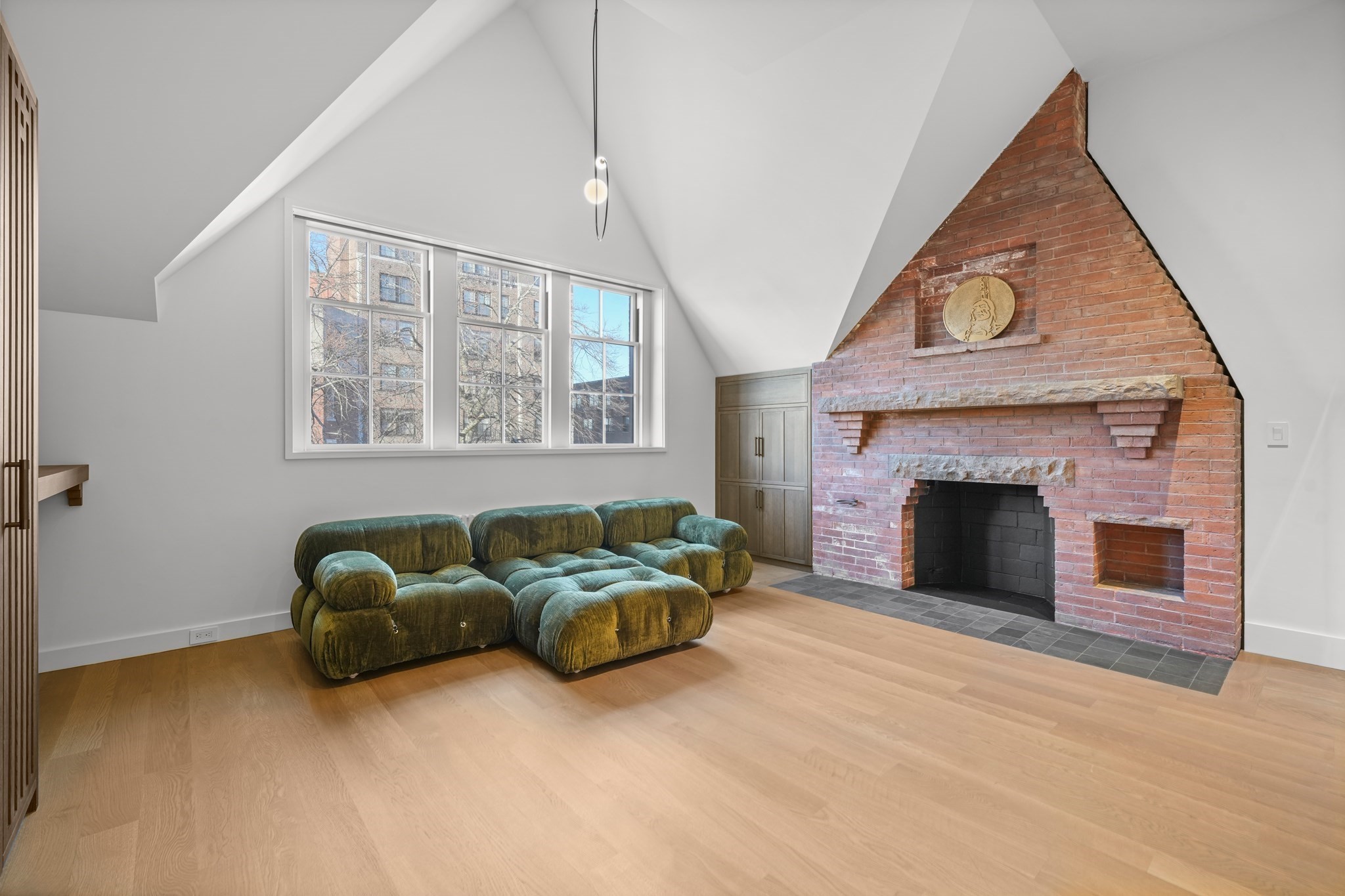 Living room with a vaulted ceiling, green modular sofa, large windows, and a prominent red brick fireplace.