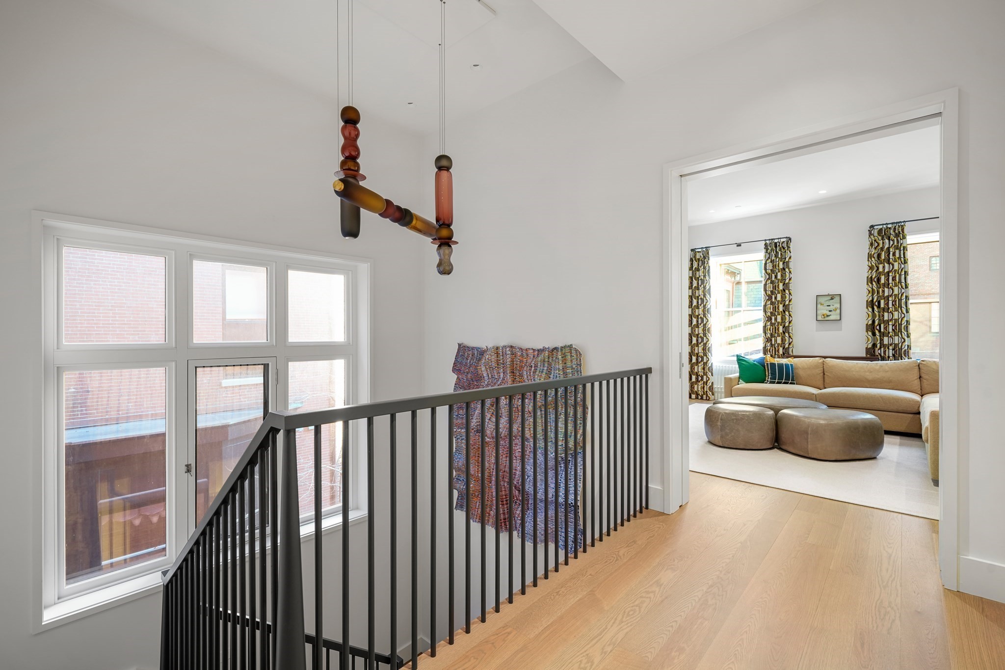 Bright stair landing with black railing and sculptural pendant, opening onto a living room with a tan sectional.