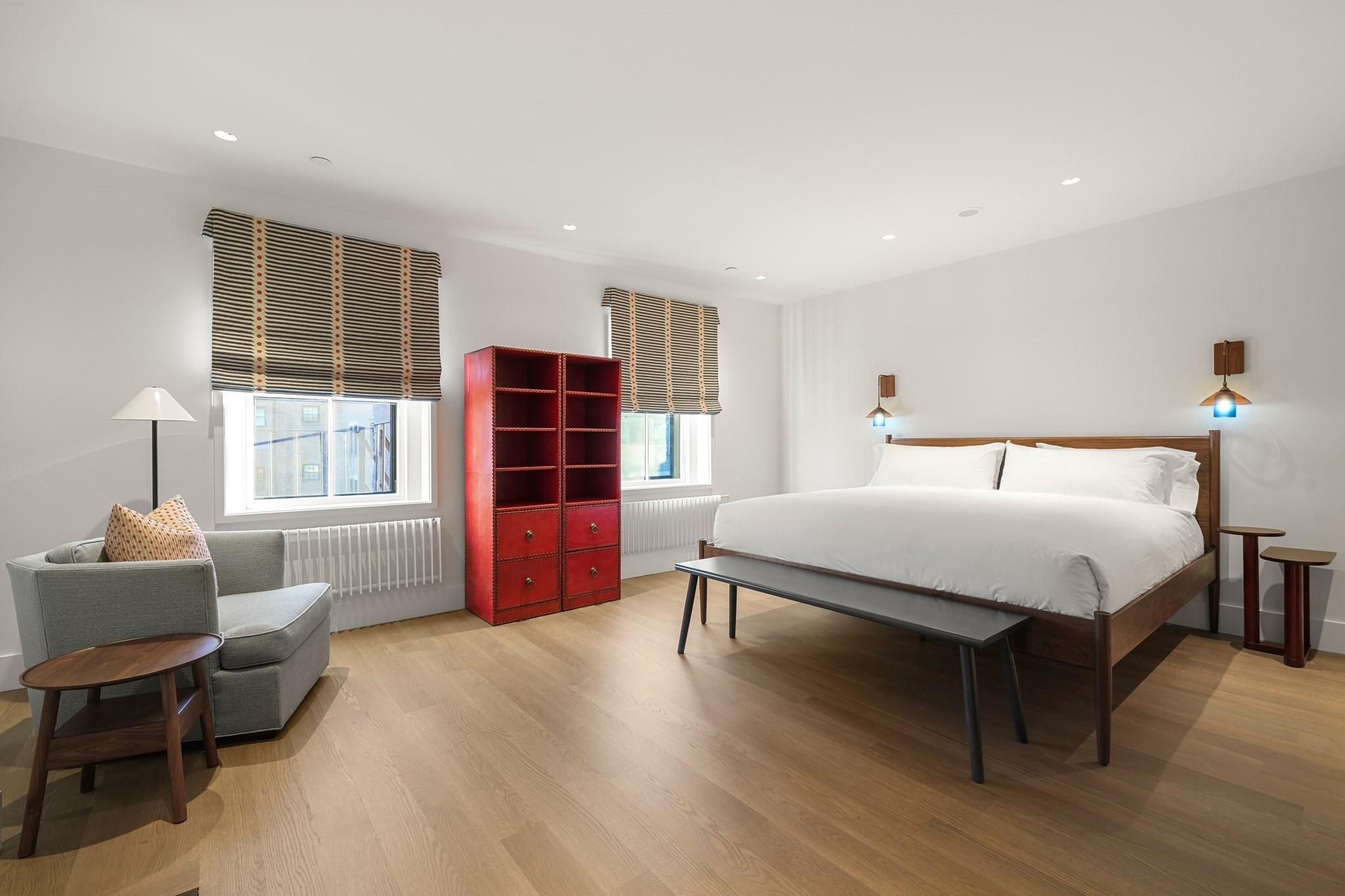 Bedroom with a white bed, gray armchair, and red shelving cabinet.