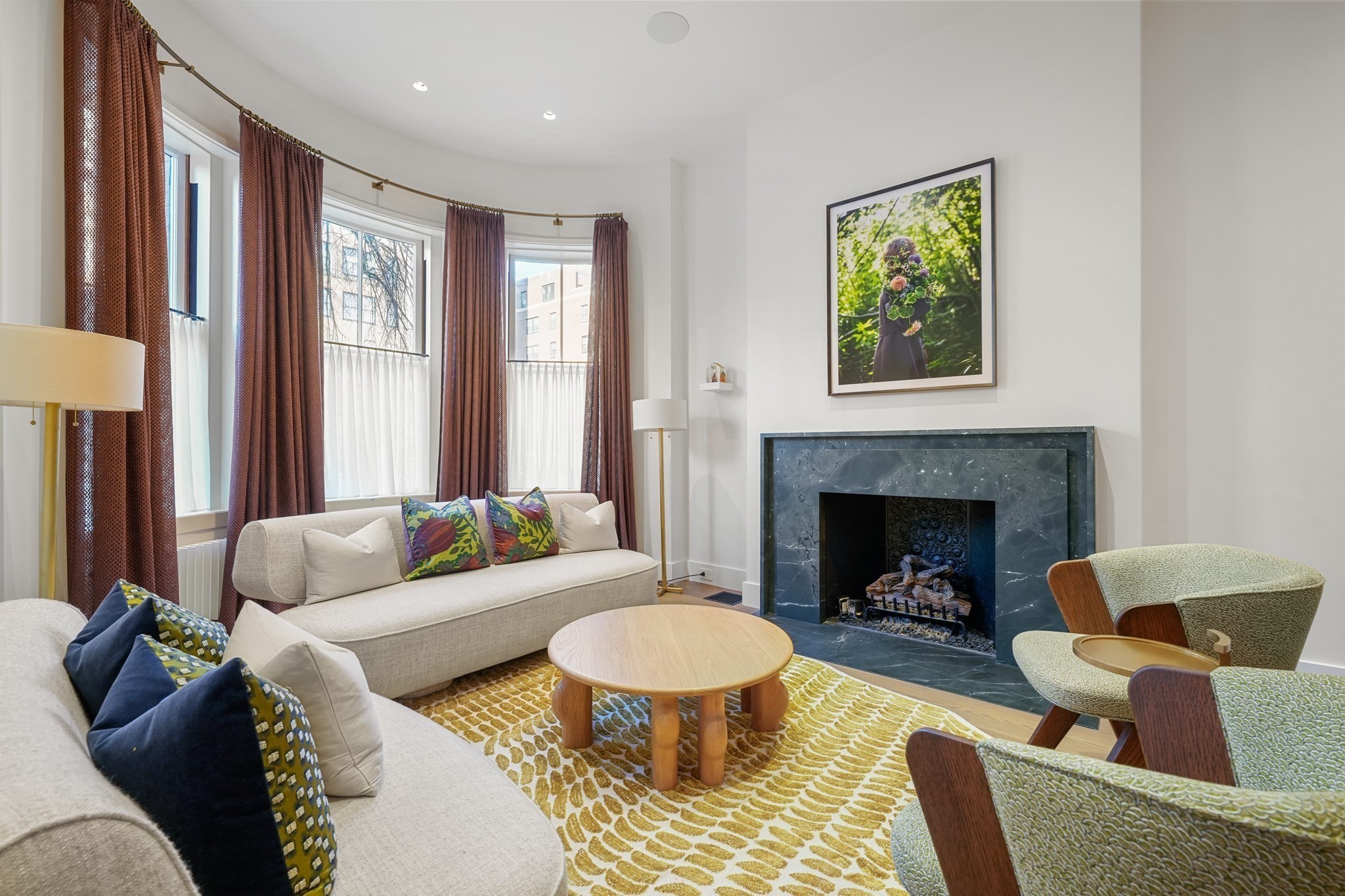 Living room with a curved bay window, cream sofas, patterned chairs, and a marble fireplace.