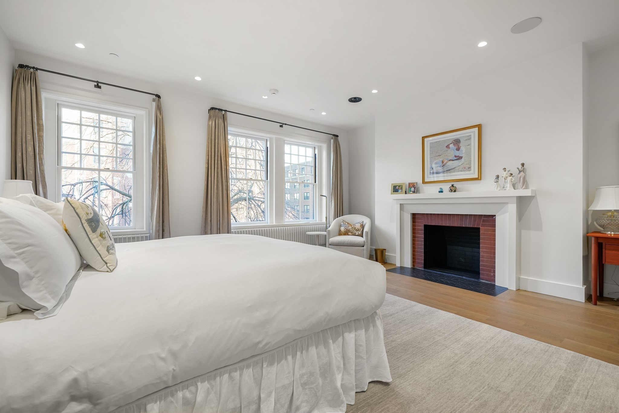 Bedroom with a white bed, tall windows, and a brick fireplace beneath a white mantel.