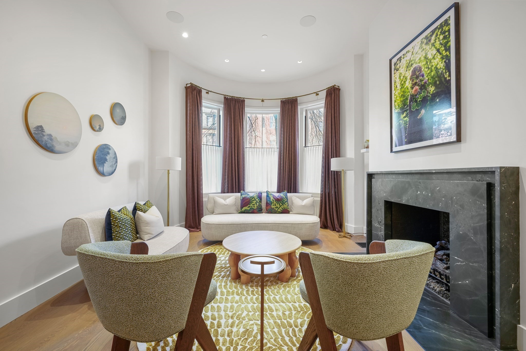 Living room with a curved bay window, marble fireplace, and patterned rug.
