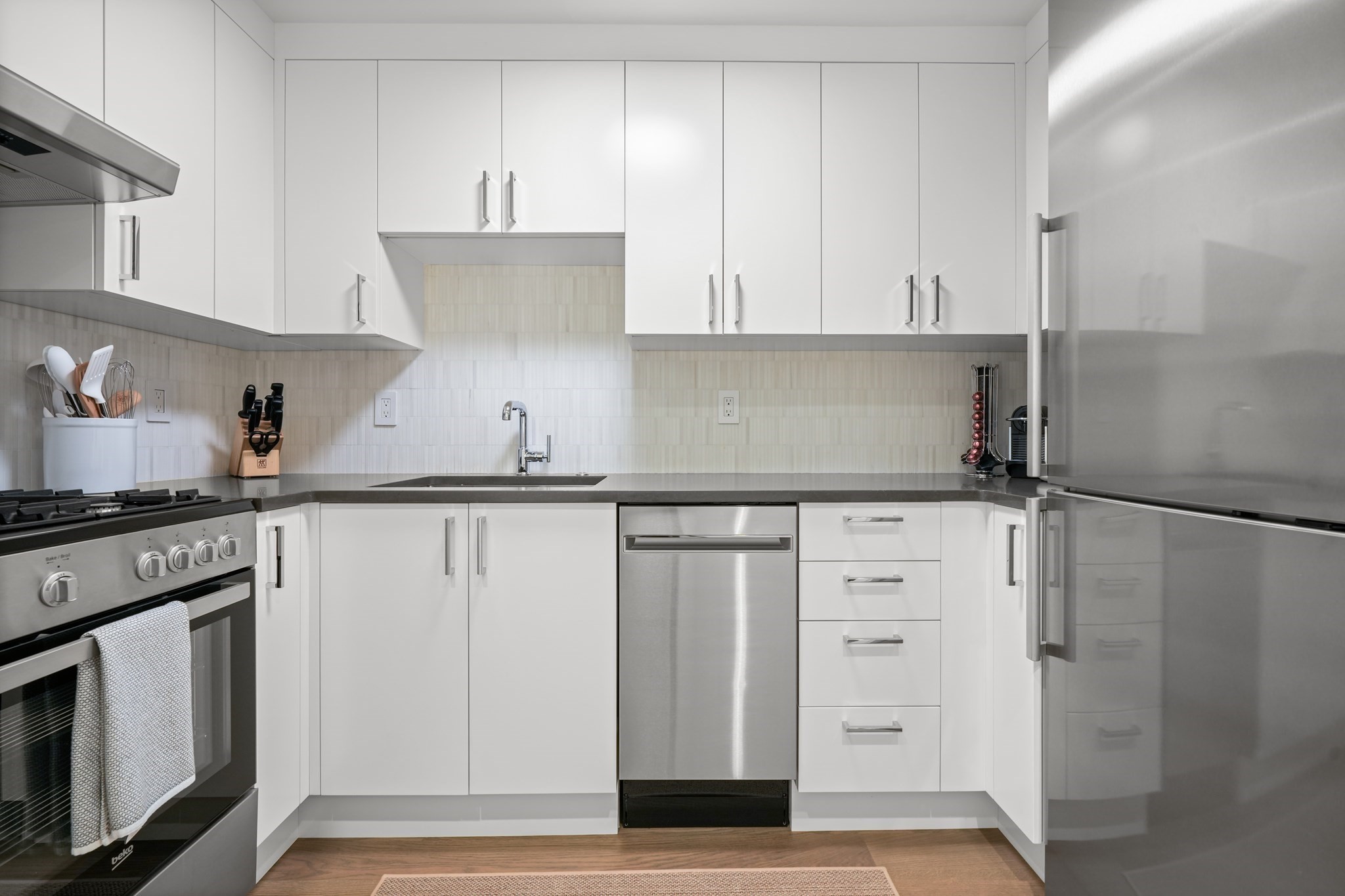 Modern white kitchen with stainless steel appliances, dark countertops, and a light tile backsplash.