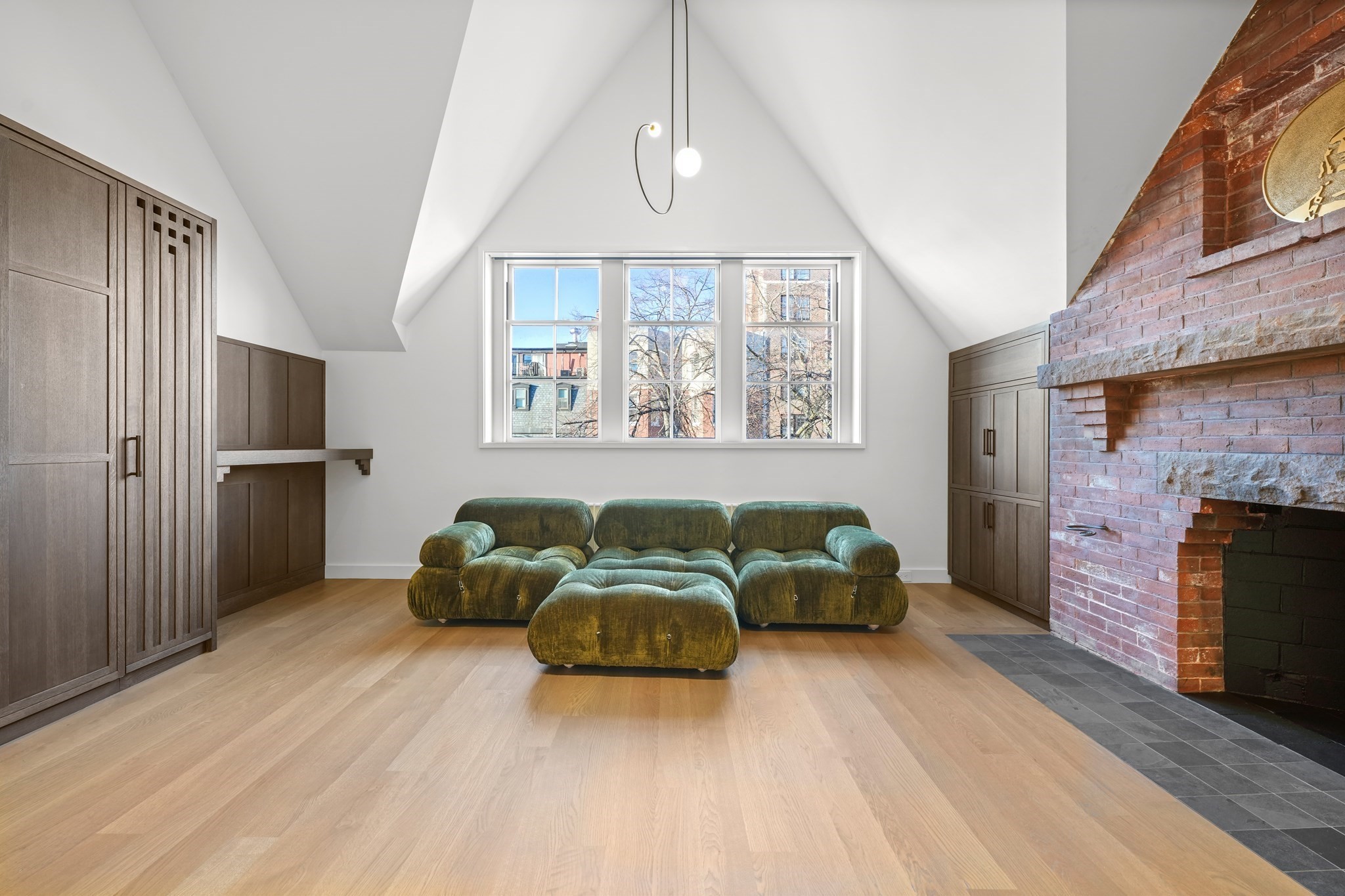 Living room with a green modular sofa, vaulted ceiling, dark wood built-ins, and a large brick fireplace.