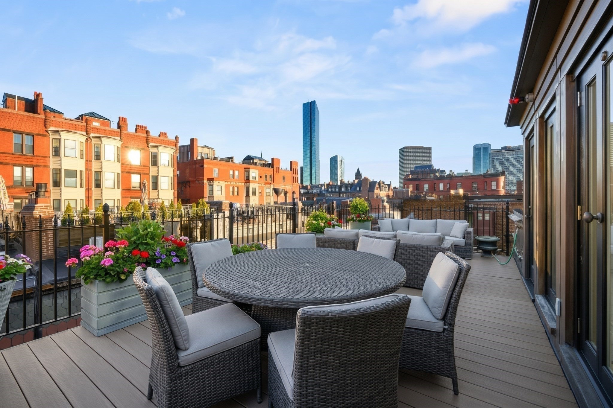 Furnished rooftop deck with wicker seating, flower planters, and Boston skyline views.