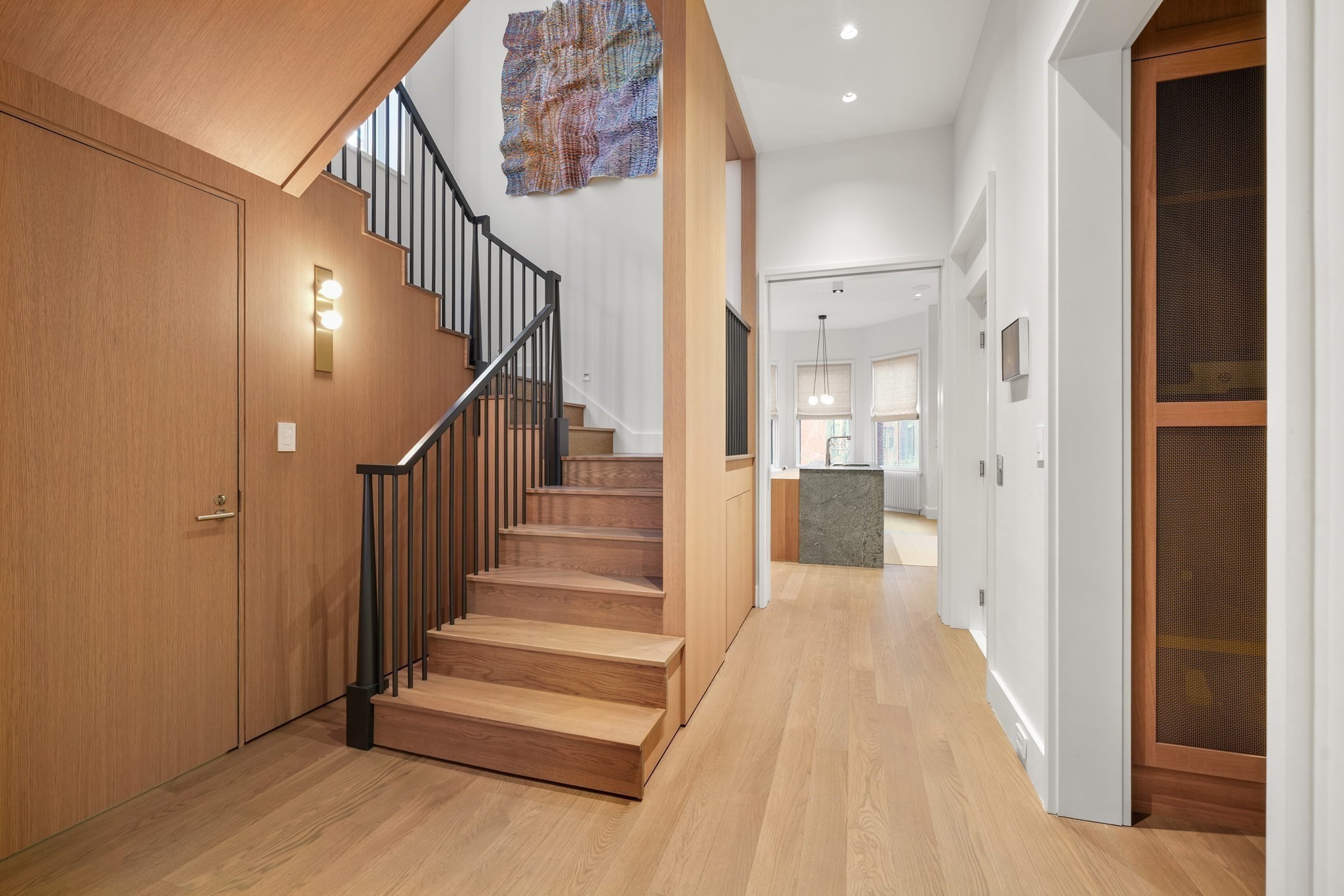 Entry hall with a wood staircase, black railings, and a view into the kitchen.